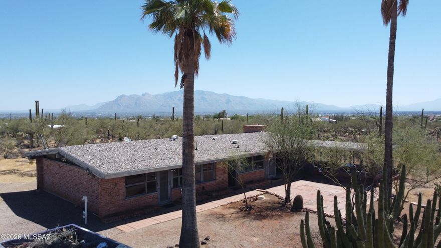 Classic Old Tucson dude ranch charm defines this private mountain retreat. Tucked away on a pristine 4.6-acre lot, the solid 1,800 sq ft masonry home is completely enveloped by mature saguaros and lush desert vegetation. Inside, multiple large picture windows frame sweeping city and mountain views around a central brick fireplace. The light-filled rustic layout features classic woodwork and built-ins throughout the space. Enjoy quiet morning coffee on the screened sun porch or step out to the separate detached auxiliary office, ideal for working from home. The expansive acreage allows plenty of room for horses with no HOA, yet sits just a short, convenient drive from I-10, shopping, and downtown. Well-preserved and sturdy, this property offers a rare opportunity for its next steward to add add their own personal touch while honoring its original character.