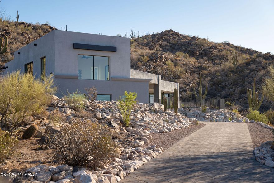 Set against the dramatic backdrop of the Tortolita Mountains, this newly completed residence is located in a private, gated enclave of just thirteen homesites, offering a rare opportunity to live immersed in the desert landscape while enjoying refined modern luxury. Perched above the Tucson Valley with sweeping views of the surrounding mountain ranges, the home was designed for those with a discerning eye for quality, craft, and connection to place.

Constructed in 2025 with energy efficiency at its core, including insulated concrete form (ICF) construction, high-SEER HVAC systems, High performance doors & windows - this residence offers year-round comfort, quiet, and enduring performance. Upon entry, a soaring foyer introduces the home with drama and restraint, setting the tone for what unfolds: a thoughtfully composed interior with a seamless connection to its natural surroundings.

A split-level design allows for a refined balance between scale and intimacy with 16-foot ceilings in the living room, 12-foot ceilings throughout the main level, 10-foot ceilings in the upper level bedrooms and bath. Each space is positioned to capture light, frame views, and flow effortlessly to the outdoors.

The heart of the home is the kitchen, a striking composition of solid surface countertops, custom walnut cabinetry, a steel-clad hood, and a suite of Sub-Zero and Wolf appliances. A walk-in butler's pantry offers generous storage, a wine fridge, and space for further customization. Two distinct living areas add a grounded elegance, spaces designed as much for entertaining as for quiet evenings spent relaxing at home. 

The main suite is a private sanctuary, with sliding doors opening directly to a covered patio with a resort-style pool and an elevated spa. A corner window wraps the bedroom in morning light, and the generously sized bathroom offers natural illumination and intimate views of the desert beyond. 

Four additional en-suite bedrooms are well-placed for privacy and ease of movement throughout. At the upstairs, a private patio off the bedrooms offers a quiet perch to take in the long-range views, city lights by night, mountain silhouettes by day. Built-ins and ample closets are thoughtfully integrated throughout the home, ensuring that storage is as functional as it is discreet.

Outdoor living is an extension of the architecture: the main covered patio includes a built-in outdoor kitchen, perfect for entertaining beside the pool and spa, while shaded porches, dining terraces, and lounging areas are positioned to take full advantage of the sun, shelter, and expansive desert views. All of the outdoor spaces are shaped by the surrounding natural topography and designed to enhance both solitude and connection. 

Ideally located near luxury resorts, restaurants, shopping, hiking trails, and award-winning golf. Minutes from T Bench Bar, two premier golf destinations await. Stone Canyon - a private 1,400 acre community in Oro Valley is ranked among Golf Digest's "Top 100 in America," along with a luxury fitness center, upscale dining, and year-round social events. The Clubs at Dove Mountain combine The Gallery Golf Club and The Golf Club at Dove Mountain, offering two exceptional courses and a single membership in a stunning desert setting. Minutes to I-10 with excellent access to both Tucson and Phoenix airports, this is desert living at its most elevated.