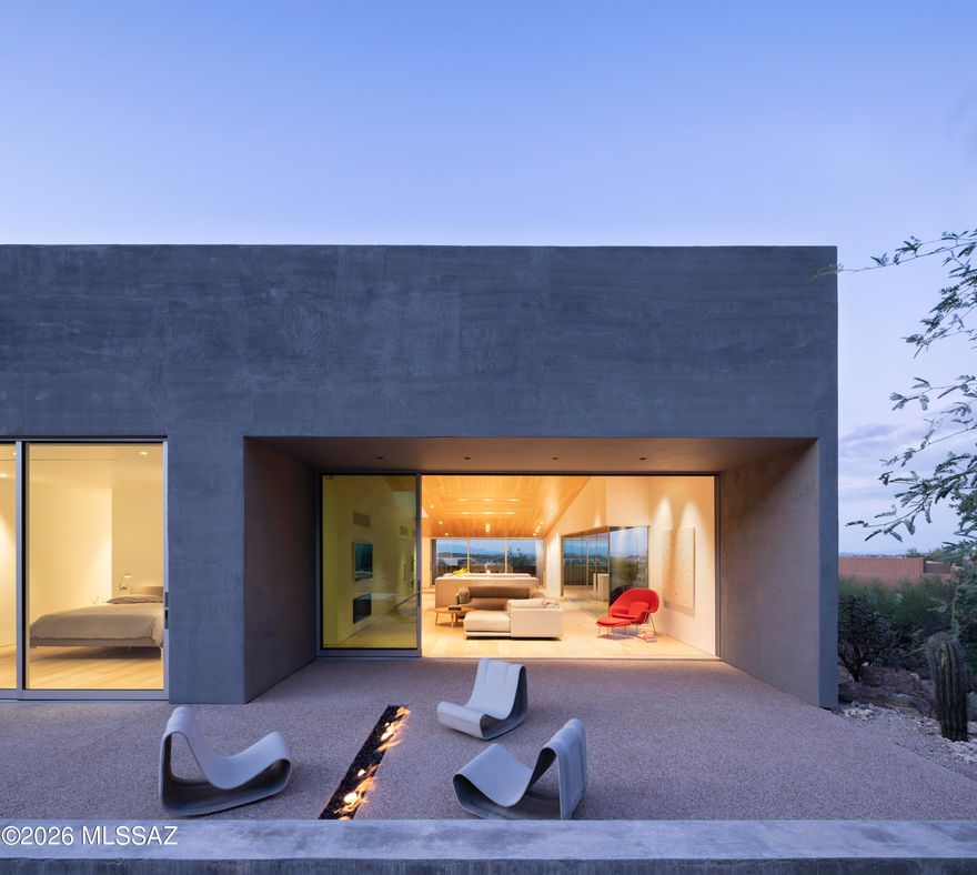 Ventana House rises from the sloping Sonoran Desert terrain, its forms grounded, sculpted, and elemental. Walls of textured material and deep apertures frame the landscape, mediating between exposure and refuge, allowing the desert to be experienced as a composed and measured extension of the architecture. Light, shadow, and space are orchestrated to reveal the environment slowly, with a sense of discovery around every corner. Designed by the renowned architectural firm HK Associates, the residence reflects the studio's disciplined approach to materiality, light, and form. The home has been featured in numerous international architectural publications, including Wallpaper Magazine, ArchDaily, dezeen, among others, underscoring its significance within contemporary desert modernism. The home unfolds as a sequence of calm, luminous spaces defined by precision and restraint. A double height entry gallery is washed in filtered daylight, while a perforated steel bridge introduces a moment of suspension before arriving at the primary living areas. Materiality throughout is refined and intentional. Plank hardwood floors extend beneath the matching wood ceilings, creating a cohesive warmth that contrasts with smooth painted walls and crisp white millwork. Mechanical elements, ventilation grilles, and lighting are recessed and aligned to preserve visual quiet.

The upper level accommodates the great room, a dedicated office, the primary suite, and a secondary suite, while terraces extend outward through expansive recessed glazing, softening transitions without overstating the connection. Living and dining spaces are situated beneath a sloped wood ceiling clad in wide plank boards that echo the contours of the foothills beyond. Integrated linear lighting and recessed fixtures are set flush within the ceiling plane, reinforcing continuity while modulating light throughout the day.

Kitchen and baths are articulated with slab front millwork, concealed hardware, and integrated monolithic surface countertops with precision edges and minimal shadow line reveals. In the primary bath, ribbed wall tile, large format flooring, frameless glass, and integrated surface vanities create a spa-like environment defined by texture and clarity.

The lower level is equally considered, housing an oversized three car garage, gym, office, den, laundry, and a third ensuite bedroom, each space composed to support both function and flow. Throughout, detailing is exacting, with tight tolerances and an emphasis on proportion and alignment.

Set within the guard gated enclave of Ventana Country Club, the home is complemented by access to world class club amenities and a network of nearby hiking trails that trace the foothills of the Catalina Mountains. These surroundings provide a natural counterpoint to the architecture without competing for attention, reinforcing a lifestyle that values both leisure and quiet immersion.

Ventana House is a modern desert retreat defined by clarity, restraint, and enduring craftsmanship - a residence where material integrity and architectural precision take precedence, allowing the landscape to be present, measured, and timeless.