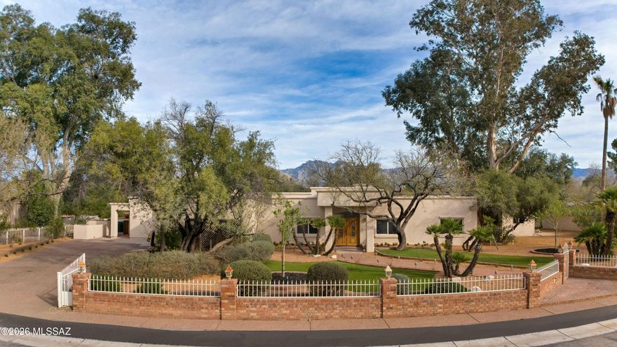 Introducing a rare opportunity within the prestigious, gated community of Tucson Country Club Estates. Offered for the very first time, this exceptional residence has been lovingly cared for by one family and is gracefully positioned on a lush and private .66-acre homesite framed by mature trees, gardens, and manicured low-maintenance turf, all secured by a charming brick with white iron fence accents and a gated driveway.
A welcoming covered porch with wood plank ceiling and double doors sets the stage for the warm, inviting interiors beyond. Inside, soaring ceilings, rich wood flooring, and timeless architectural details define the gracious living room, anchored by a gas fireplace and designed for entertaining and everyday comfort.
At the heart of the home, the expansive kitchen offers extensive cabinetry and dual granite islands; one functioning as a breakfast bar seamlessly opening to the cozy family room and sunlit breakfast nook, enhanced by a gas fireplace, creating an atmosphere of connection and warmth.

Thoughtfully designed for flexibility and privacy, the separate guest quarters include a living room, kitchenette, private bedroom, and bath, with direct access to both the backyard and driveway, ideal for guests, extended family, or multi-generational living. A spacious addition, previously enjoyed as a teen retreat, offers versatility for a game room, media lounge, or creative studio, complete with its own ½ bath.

The private bedroom wing features a handsome den with custom built-in bookcases and a desk, three generously sized bedrooms, and a serene primary suite with its own fireplace, walk-in closet, and spacious bath featuring dual split vanities, a soaking tub, and a separate shower.

The backyard is a true sanctuary, highlighted by a sparkling pool, a rock waterfall, an attractive three-tier fountain, and multiple fenced areas for recreation. A north-facing covered patio and a new built-in stainless-steel barbecue create the perfect setting for outdoor gatherings year-round.

Additional amenities include a detached, climate-controlled fitness room, abundant storage, and expansive side yards.
Tucson Country Club Estates is celebrated for its welcoming sense of community, offering neighborhood gatherings, parades, and peaceful streets ideal for walking and enjoying the surrounding beauty. With no HOA, this is a rare offering that combines privacy and an exceptional lifestyle.