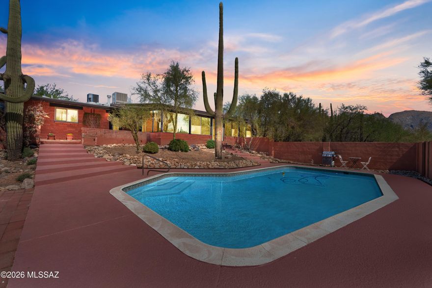 Classic mid-century modern architecture meets thoughtful, high-end reimagination in this exceptional 1963 adobe set on a private .88-acre lot in the Catalina Foothills. With 4 bedrooms, 3 bathrooms, and 2,779 square feet, the home has been meticulously updated while honoring the clean lines and warmth of true MCM design. An understated exterior gives way to beautifully carved double wood doors, clerestory windows, and light-filled interiors. The inviting living room is anchored by a striking masonry wood-burning fireplace that contrasts perfectly with the home's architectural simplicity and flows seamlessly into the main living spaces. The kitchen is a true focal point, featuring custom exotic wood cabinetry crafted from a single tree specimen, white quartz countertops, and a waterfall-edge bar. A breakfast nook with pass-through window and views of the family room, backyard, and pool keeps the space open and connected, ideal for entertaining. The converted Arizona room offers year-round enjoyment with views of downtown Tucson and A Mountain. New dual-pane windows, a sliding glass door, and a whisper-quiet mini-split create a comfortable space for morning coffee, evening dining, and relaxed gatherings. Three guest bedrooms are thoughtfully arranged along the hallway, along with a beautifully updated bathroom that functions as a pool-ready wet room with direct backyard access and interior laundry. The primary suite is a serene retreat with backyard and pool access and a stylishly updated primary bath. Every detail has been carefully curated to preserve the home's mid-century soul while delivering modern comfort and timeless appeal. A rare Catalina Foothills offering.