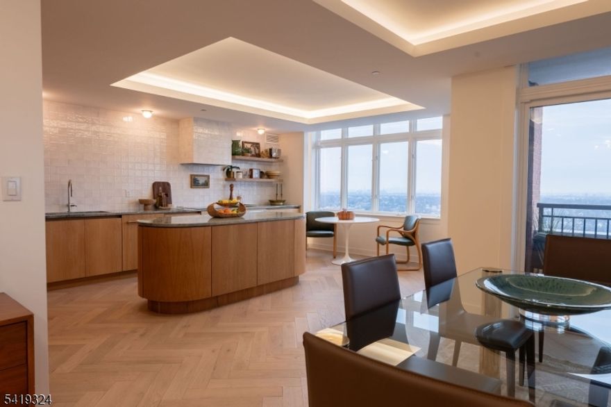 Perched at The Top, SOMA's premier luxury condominium, this fully renovated 3-bedroom residence showcases elevated design, exceptional craftsmanship, and sweeping NYC skyline views. Thoughtfully reimagined with a full designer renovation, every surface and finish has been curated with exceptional taste and attention to detail. An east-facing exposure fills the home with beautiful natural light throughout the day, enhanced by expansive windows and a seamless indoor-outdoor connection to a private balcony. New flooring laid in a sophisticated herringbone pattern, paired with sound-reducing underlayment, adds both style and comfort underfoot. Each of the three spacious bedrooms features its own ensuite full bath. The primary suite features a dressing area and bath with a soaking tub, stall shower w/new glass door, and refined new tile work. A stylish powder room off the hallway is ideal for guests, while custom built-in closets throughout provide exceptional storage solutions. The showstopping kitchen features custom wood cabinetry, marble counters, open shelving, and new appliances. A striking rounded center island anchors the space. Thoughtfully selected light fixtures and cove lighting on dimmers create the perfect ambiance throughout. Boasting one of the largest floorplans in The Top at 2500+ sqft, this home offers refined suburban living in the vibrant heart of Essex County, just moments from everything South Orange and Maplewood have to offer.