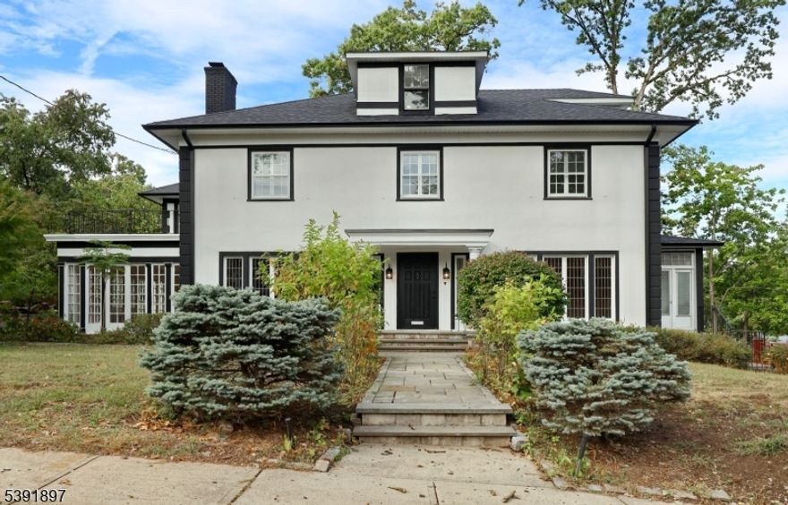 Discover timeless character in this French Colonial-style Center Hall home, ideally situated in Paterson's prestigious Manor Section. Built in 1928, this residence offers nearly 4,000 sq ft of elegant living space filled with light, warmth, and architectural charm. Originally home to French diplomats commuting to New York City's French Embassy, the property also holds a place in local history - President Gerald Ford once attended a dinner party here, adding to its quiet prestige and storybook past. Inside, the home features 10 spacious rooms, including a living room and sunroom connected by a shared fireplace, creating cozy, flowing spaces perfect for both everyday comfort and entertaining. The updated kitchen features marble flooring, new stainless-steel appliances, and tasteful modern finishes that harmonize beautifully with the home's original details. The primary suite offers four closets and a luxurious renovated bath, while additional bedrooms are bright and well-proportioned. A distinctive ballroom/library provides an inspiring space for gatherings, music, or a home office. Throughout the home, hardwood floors, antique lighting, and original window craftsmanship reflect its authentic 1920s character. The full, partially finished basement, once used as a flower workshop, offers versatile options for a studio, art or model-making space, or gym. A 5 car garage w/ direct entry beneath the home adds convenience.