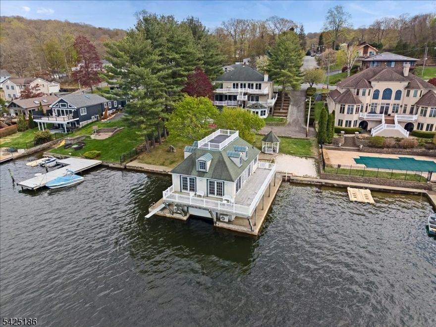 Welcome to this exceptional lakefront Colonial in the sought-after Great Cove section of Lake Hopatcong. Designed to maximize waterfront living, this distinctive residence spans three levels and offers a seamless blend of comfort, functionality, and scenic beauty.  The main level features a refined parlor/library with custom built-ins, flowing into an open-concept kitchen, dining area, and living room. A full rear wall of sliders invites natural light and captures expansive lake views, creating a true indoor-outdoor experience. Multiple decks on each level further enhance the home's connection to the water.  The residence includes five spacious bedroom suites, each with private baths and generous closet space, including walk-ins. In total, the home offers six full bathrooms and one powder room. The ground level is well-suited for entertaining, complete with a secondary kitchen, recreation space, and game area and 3 season room. Additional highlights include two separate garages accommodating four or more vehicles. Complementing the main residence is a beautifully crafted custom boathouse featuring two additional bedrooms, two showers, and two commodes, all fully equipped with heat and central air.  This rare offering is further enhanced by grandfathered dual cement docks, a private beach, and a lakeside gazebo delivering a complete lakefront lifestyle.