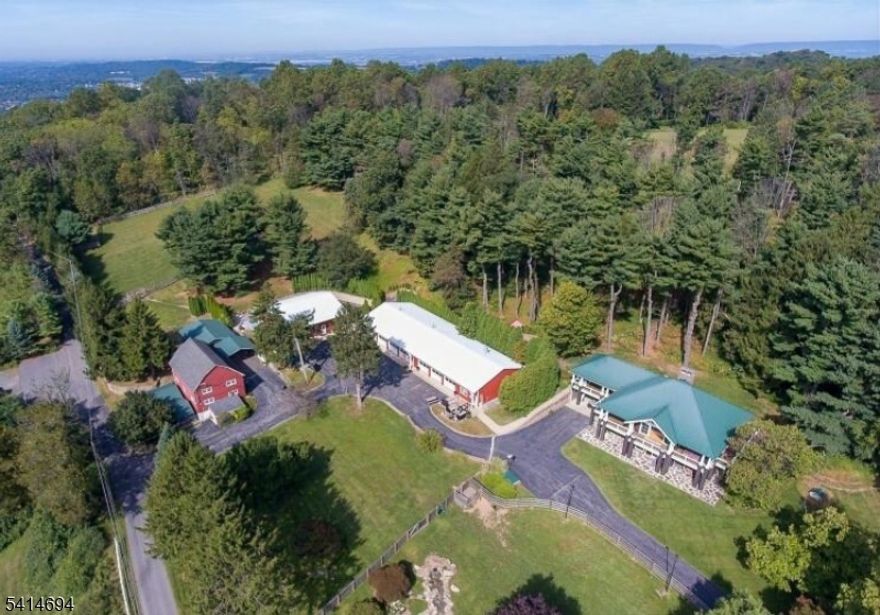 This exceptional 18-acre estate presents a myriad of opportunities for its future owner. Constructed in 2008, the custom Colonial home encompasses 3,600 square feet and features a welcoming open floor plan that highlights stunning 50-mile vistas from its wraparound covered verandas. Inside, the residence is adorned with two full-wall custom fireplaces, a great room with soaring vaulted ceilings, and elegant maple hardwood floors throughout. The gourmet kitchen is a chef's dream, boasting exotic granite countertops, custom cabinetry, a spacious island, and professional-grade appliances, all seamlessly connected to the dining area. The main level hosts a luxurious primary bedroom suite with a generous walk-in closet, along with a great room, dining room, laundry, and mudroom. The lower level offers two large ensuite bedrooms, a living room, a covered patio, and a private entrance, making it ideal for separate living areas. Additionally, this property caters to car enthusiasts and those interested in Airbnb ventures, featuring a 40x50 former kennel building with a guest room and full bath, a historic three-level bank barn, and a 40x112 auxiliary building with seven bay garages and a reception area. With two full-house generators, a small pony barn, and open fields, this expansive estate also includes the potential for a separate seven-acre building lot. Conveniently situated near major highways and shopping, this property is truly a rare find.