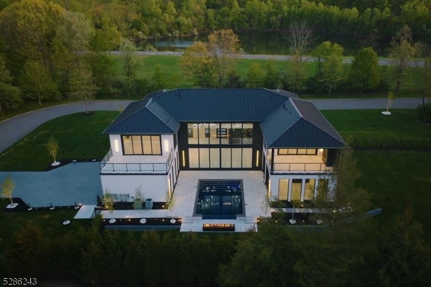 This architectural gem featuring 5 bedrooms, 7 full and 1 half bath radiates modern elegance. Its grand entrance showcases a stunning pivot door, revealing a light-filled foyer with towering windows. The two-story great room boasts panoramic views and flows into a state-of-the-art kitchen. A highlight of this home is a 3-story floating staircase crowned with a 28-foot chandelier. The property features a luxurious primary suite that offers unparalleled privacy, a spa-like bathroom, spacious walk-in, and a private balcony. The second floor features four additional luxe ensuite bedrooms. Outside is a custom pool backed by a fire pit lounge.