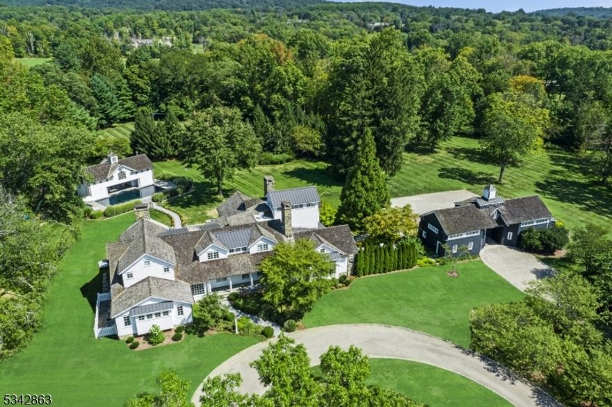 Tucked away in the picturesque landscape of Far Hills, within an hour of NYC, this extraordinary country estate provides an exquisite blend of rustic charm and modern luxury. Set on 10+ gated acres, this private retreat offers natural beauty, architectural excellence, and refined craftsmanship. An extensive 2005 rebuild resulted in a stunning 6-bedroom residence. The spacious home, with two 1st-floor suites for guests, is defined by hand-crafted millwork and hardwoods that adorn the interior. The newly updated chef's kitchen features radiant-heated floors, state-of-the-art appliances, custom cabinetry, and a breakfast bar. The adjacent great room, crowned by soaring hand-hewn beams, serves as the heart of the home, with a floor-to-ceiling stone fireplace and walls of windows that invite in natural light. The primary suite is a serene retreat, complete with a tower office with breathtaking views of the estate's gardens and rolling lawns. The deer-fenced property includes a pool, pool house, tennis court, reflecting pond with fountain and entertainment patios with a hot tub & outdoor kitchen. The carriage house presents a 4-car garage, office, gym, and full bath. This extraordinary home showcases an exterior of fieldstone, hand-split cedar roofing, copper gutters, fieldstone chimneys, and covered porches. Far Hills offers a coveted lifestyle with its equestrian heritage, scenic countryside, world-class golf courses, top-rated schools, fine dining, and access to NJ Transit.