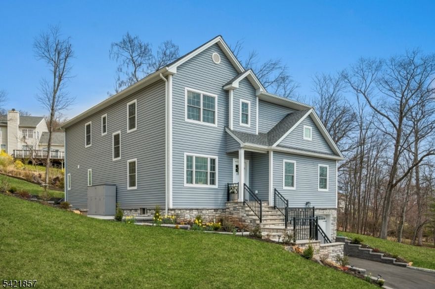 A 2025 build, taken beyond builder-grade by the current owners. Six bedrooms, four and a half baths, approx. 4,400 finished square feet on a private double lot running up to Washington Rock State Park, with direct trail access. Perched on a quiet elevation with sweeping views, the home opens into a bright family room with white oak floors and nine-foot ceilings. A chef's kitchen with quartz-topped island and walk-in pantry flows off it, alongside a dining room with crown molding and a living room with gas fireplace. A first-floor bedroom with its own full bath, private enough for guests and quiet enough for a home office. Upstairs, the primary suite with soaking tub and walk-in shower is joined by three additional bedrooms, a full bath, and second-floor laundry. The finished lower level adds a sixth bedroom with its own full bath, plus open flex space. What sets this home apart: the post-build work. Stone veneer wraps the exterior. The back stairs were rebuilt in stone with new railing to match the front elevation. A paved patio with a French drain anchors the yard, and a paved path circles the house to a dedicated trampoline area. New sod and trees complete the landscaping. Hardwood floors sanded and refinished. Two walk-in closets added. Garage floor coated. New appliances throughout. EV-prewired two-car garage, 200-amp service, Watchung Hills Regional HS. Eight minutes to Dunellen station. Move-in ready, every major upgrade done, inside and out.