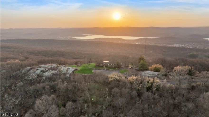 A one-of-a-kind mid-century modern with an unmistakable Hollywood Hills sensibility, set high along the ridgeline of the Ramapo Mountains at the end of a nearly mile-long cul-de-sac, surrounded by an expansive protected mountain landscape, with panoramic views spanning the Wanaque Reservoir, the surrounding range, and the New York City skyline.The only residence at the end point, the home is defined by its position, elevation, and perspective. Built in 1960, it was designed around the view, with walls of glass, a double-sided fireplace, and original knotty pine tongue-and-groove paneling and ceilings defining the main living spaces. Period-specific elements remain intact throughout, reflecting the home's original mid-century design and reinforcing its architectural consistency. A glass-enclosed indoor pool sits directly along the primary view line, fully exposed to the landscape beyond. It is a defining architectural element of the home and central to its original design. Five bedrooms and two full baths, along with a greenhouse, large workshop, attached four-car garage, and an additional open garage structure below, complete the property. Set above the surrounding landscape, the setting offers a high degree of privacy and separation, with New York City within easy reach.