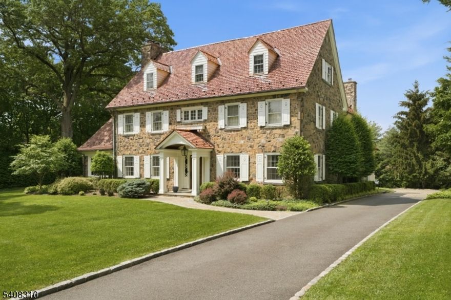 Situated on nearly an acre in Old Short Hills, this timeless fieldstone Colonial offers a rare balance of architectural significance and livability. From its classic facade to elegant proportions, the home invites you in with presence and warmth. Inside, a wide entry sets the tone. The living room, anchored by a wood-burning fireplace, flows into a sunroom with three stone walls and its own fireplace, offering a year-round connection to the outdoors. Light fills the formal dining room through multiple exposures, while a coffered ceiling adds refinement. A butler's pantry opens to a large kitchen designed for both form and function, with custom cabinetry, professional appliances and a breakfast room framed by stone and windows. French doors open to a bluestone patio and a backyard with room for a pool. A vaulted family room with exposed beams brings volume and ease, while a private office, mudroom and powder room complete the first floor. Upstairs, the primary suite offers a quiet escape with a spa-like bath and a custom walk-in closet. Three more bedrooms include two with en suite baths and one with an office. The third level continues with three bedrooms, two full baths and a lounge with versatility. The lower level includes a recreation room, gym, walk-in wine cellar and powder room, adding flexibility to any lifestyle. With a new cedar shake roof and a setting just blocks from town and the train, this is the rare home that pairs tradition with possibility inside and out.