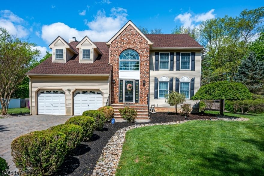 Distinguished brick-front Colonial with vinyl siding, beautifully set on a professionally landscaped property with custom paver driveway, underground sprinklers, and exceptional resort-style outdoor living. This 4-bedroom, 2.5-bath residence features a dramatic 2-story foyer, hardwood flooring throughout most of the home, formal dining room with crown molding, and a spacious family room with wood-burning fireplace. The kitchen is appointed with custom oak cabinetry, custom oak hood, center island, ceramic backsplash, Bosch dishwasher, stainless steel appliances, ceramic flooring, recessed lighting, separate breakfast area, and an arched window overlooking the backyard. Sliders open to an expansive multi-level treated deck, approx. 700 sq ft, overlooking the L-shaped in-ground pool with diving board, lighting, and vinyl liner. The primary suite offers vaulted ceiling, French doors, skylights, Jacuzzi tub, steam shower, granite finishes, gold fixtures, and two walk-in closets. Main bath updated with granite. Finished basement with recessed lighting and gas fireplace adds flexible living space. Additional features include 2nd-floor laundry, oversized shed, 2-car garage with automatic opener, and energy-efficient attic insulation. Ideally located near NJ Transit, Rutgers University, major hospitals, New Brunswick's acclaimed theater and dining scene, and major highways.
