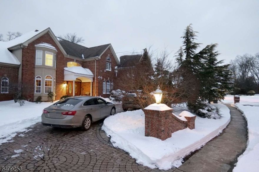 A grand three-story residence offering timeless design with modern refinement across approximately 4800 square feet, including a fully finished basement level. A circular paved driveway leads to a three gate indoor garage equipped with an electric vehicle charging setup, setting the tone for both elegance and convenience. The chandelier-accented foyer opens to sun-filled living spaces where classic proportions, thoughtful sightlines, and quality craftsmanship meet contemporary finishes. The main level features a bright sun room, formal dining and recreation areas, a spacious lounge with floor-to-ceiling windows, and a large island kitchen with marble countertops and a gas-powered stove. A flexible office or bedroom, a guest bathroom, garage entrance and a thoughtfully designed rear entry lead to an expansive outdoor retreat with patio, grill area, gazebo, and a serene pond. The second level showcases an exceptional primary suite with a private den, two walk-in closets, and a spa-inspired bath with toilet room, jacuzzi, and walk-in shower. Three additional bedrooms, two additional full baths, and generous storage complete the rest of the floor. The fully built lower level offers interior and garage access, ideal for independent living, featuring two bedrooms, one with walk-in closet and bath, a lounge, dining area, laundry room, and ample utility storage. A refined blend of traditional architecture and modern luxury, designed for scale, comfort, and elevated living.