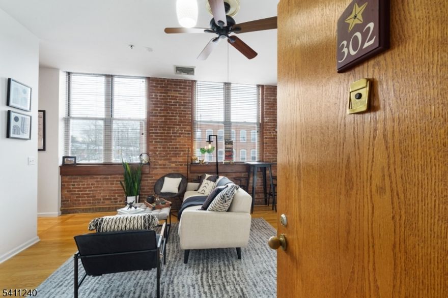 Exposed brick, soaring ceilings, and oversized industrial windows define this thoughtfully designed studio at The Mill. Authentic loft character pairs seamlessly with clean, modern finishes, creating a space that feels both warm and refined. The open living area is anchored by rich hardwood flooring and framed by classic timber window sills. A sleeping area is tucked neatly into the layout, offering separation while maintaining the airy feel. The kitchen is finished with warm wood cabinetry extending to the ceiling, providing generous storage rarely found in a studio layout. Stainless steel appliances, a sleek black subway tile backsplash, and neutral countertops create a clean, contemporary contrast against the exposed brick. Storage is a true highlight. Large closet, including a spacious wardrobe with overhead shelving, offer substantial organization capacity, while the in-unit washer and dryer are conveniently tucked behind louvered doors for everyday ease. Residents of The Mill enjoy access to a full suite of amenities including a fitness center, community room, swimming pool, tennis courts, walking and jogging paths, and a plaza deck overlooking the waterfalls. Easy access to shopping, dining, and NYC transportation completes the offering.