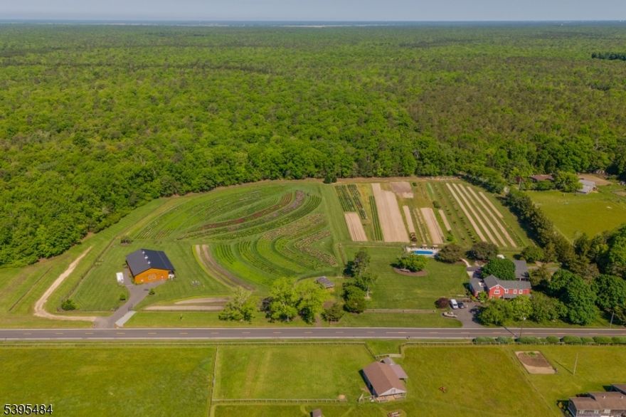 This 2011 custom home sits on 17.25 acres bordering Belleplain State Forest and is approximately 15 minutes from the new Trout National Golf Course. Direct forest adjacency provides access to the trail system about 1.5 miles away. The main level features hardwood floors, an open kitchen, dining area, a sitting room and living room with a dual wood-burning and gas fireplace. A first-floor guest suite includes a full bathroom and wet bar. The second floor offers three additional bedrooms plus a nursery/office with its own closet off the primary suite. Upgrades include a 400-amp electrical service (200A house / 200A barn), whole-house generator, and two HVAC systems (1st-floor unit 1 year old), and new french drain and concrete flooring in the basement. The heated in-ground pool is fully fenced, and the flower fields have deer fencing. The 26 60 barn (built 2019) has concrete flooring with a removable wood overlay for easy conversion to stables. Detached garage/carriage house was built in 2013. Approximately 20 minutes to Sea Isle City, Stone Harbor, and Avalon, and 15 minutes to Woodbine Municipal Airport. Video tour available!