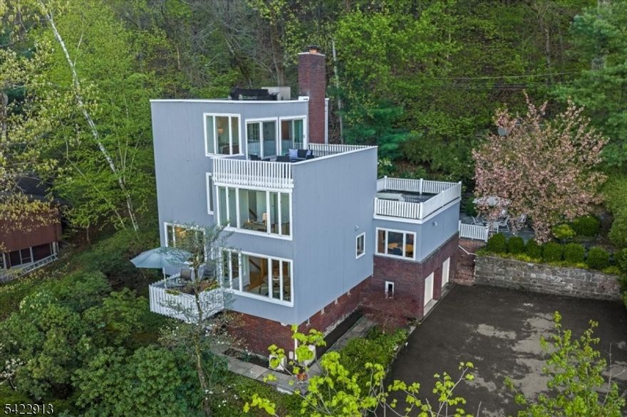 Perched high above Upper Montclair, this 5-bedroom, 3 1/2 bath, 1960 contemporary offers what may be the most extraordinary view of the New York City skyline in the entire region - visible from nearly every room, unobstructed, panoramic, and alive in every season. Surrounded by treetops, with the privacy and feeling of the Hollywood hills, it is a genuine sanctuary. At sunrise the skyline glows. At dusk it becomes a constellation of light. No neighboring roofline interrupts it. No future development threatens it. Inside, the home matches the view - warm, confident, and built to last. The expansive living room features a wall of windows framing the skyline and a wood-burning fireplace. A front deck and formal dining room share the same sweeping views. The kitchen, with its own eating area and adjoining family room - all with heated floors - create an easy rhythm for daily life and entertaining. The primary suite claims an entire floor of the home, offering a second wood-burning fireplace, wall of closets, en-suite bath with double vanity and walk-in shower, and its own private deck. In the rear, a large bluestone patio, gardens, and another large deck - quiet, private, and entirely your own. Laundry on the bedroom level. Beautiful hardwood floors. Recessed lighting. 3-zone heat. Top floor has central A/C; mini-splits cool the rest of the home. Whole-house generator, 2-car built-in garage, irrigation. 0.8 miles to Upper Montclair train. 12 miles to Midtown.