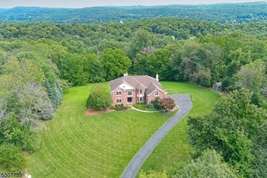 Welcome home to this little slice of heaven situated on over 4 acres just a few miles from the center of town, Route 15, and North Village. This stately home offers extreme privacy and exceptional views. Everything about the finish work in this home suggests "quality" including the exquisite hardwood floors where shown, solid wood passage doors, arched door openings, architectural ceilings, and a even bridge on the upper level offering dramatic views of the scenery outside from every vantage point. The cook's kitchen features furniture grade Cherry cabinetry and granite counters with a decorative back splash and inlaid design accent over the cooktop, double wall ovens, a B/I refrigerator/freezer, D/W, and microwave oven, and even a trash compactor. Conveniently located just footsteps away you'll find the Laundry Room with utility sink cabinet and built-in storage above. The main living space is accented by both the 2 story Entry Foyer and the Family Room with Palladium Windows. Every surface has been redone in the past 2 years. This home sets the standard for "move in ready"! Outside you find a full brick front with brick foundation walls on the sides and rear of the home and a paver stone patio on the lower level.  Enjoy the convenience of the 3 car on-grade garage located just a few steps from the kitchen. Don't miss the full finished W/O lower level with a sound insulated Media Room, Rec Room, Game Area, 2 Utility Rooms, 2 Storage Closets and a FULL BATH with stall shower.