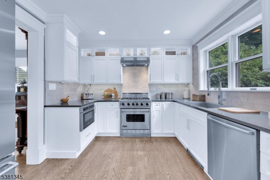 Beautifully updated home blending timeless charm with modern comforts, just steps from the train station, walking trails & outdoor concerts. Step through the covered front porch and into the foyer featuring hardwood floors, rebuilt columns, and detailed moldings. The living room offers a stone wood-burning fireplace, recessed lighting, and hardwood floors, with elegant pocket doors that open to the formal dining room. The kitchen is a chef's dream with quartz countertops, Carrera marble backsplash, white ceiling-height cabinetry, and premium Viking and Bosch appliances. A rustic barn board accent wall adds a touch of farmhouse flair, and recessed lighting keeps the space bright and welcoming. A stylishly updated powder room with a marble vanity completes the first floor. Upstairs, the primary suite features two double closets and wall-to-wall carpeting. The en-suite bathroom includes ceramic tile, a tub/shower combination, and a sleek single vanity. Three additional bedrooms share a full bath with marble countertops, ceramic tile, and a tub/shower. The finished basement offers a large rec room/playroom with three closets and an additional half bath. A walk-up attic provides additional storage. Additional features include plantation shutters, white aluminum siding, detached 2-car garage, and beautifully landscaped front gardens. This move-in ready home offers the perfect balance of character, comfort, and convenience in one of Morris Plains' most desirable neighborhoods.