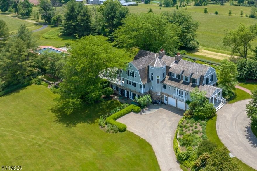 This stunning 1987 Shingle-style home was designed by renowned architect Robert A.M. Stern. The architecture has a distinct Hamptons feel on 23 farm assessed bucolic acres. A thoughtful renovation from 2017-2019 gives this 5 bedroom home a fresh, clean, modern look. Custom mill work and wood floors enhance the style of the generously sized principal rooms, ideal for entertaining. A pergola covered blue stone patio runs the length of the home and the spacious screened in porch encourages indoor outdoor living. The updated kitchen is fitted with custom cabinetry, a marble center island and stainless appliances. A magnificent circular staircase leads to both the 2nd floor and lower level. The primary suite features a bedroom with gas fireplace and screened porch. The views are breathtaking. There is also a spa-like bathroom and walk-in closet. Two additional bedrooms share a full bath and a 4th bedroom adjoins a private bath. The walkout lower level offers oversized windows and French doors to a lower garden with lots of light streaming into a rec room and 5th bedroom with bath. Also found on the lower level is a catering kitchen with huge pantry, an office with custom cabinetry and access to a 3 car garage. This property also boasts an in ground pool, tennis court, a detached "garage barn" with 5 additional bays and full house generator. Enjoy Bedminster low taxes, great school and total peace and serenity in the heart of horse country surrounded by resort-caliber amenities.