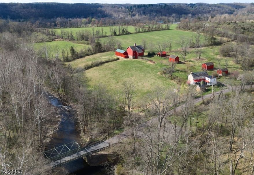One of the most intriguing parcels of land in Delaware Township, Zega Farm dates to 1798 and spans over 79 acres of rural serenity. Rolling open fields meet a quiet wooded grove along the winding Lockatong Creek, creating a picturesque landscape. This property represents one of the last large, unpreserved farms in the area. The land includes an 18th-century colonial stone farmhouse with handsome stone quoining and charming fireplaces, several farm outbuildings, and a remarkable slate-roofed bank barn. Historians note the barn's mid-19th-century construction, immense scale, and cathedral-like interior with impressive hand-hewn timbers. The exterior showcases beautiful masonry using stone in varied shapes, textures, and colors. From the drive approaching the barn, fields unfold toward the Delaware River Valley, offering unobstructed, unparalleled views of Pennsylvania's distant cliffs. Across the road lies additional meadow and woodland preserved by the Zega Historic Land Trust. The farm sits on a quiet country road with a single-lane iron truss bridge over the creek, dating to 1878 and listed on the National Register of Historic Places. Ideally located near the Delaware River and towpath, the property is close to shopping, dining, orchards, farm markets, antique and art galleries, and country inns on both the New Jersey and Pennsylvania sides of the river. It is minutes from Stockton, Lambertville, and New Hope, with approx commutes of 75 min to NYC and 60 minutes to Phila.