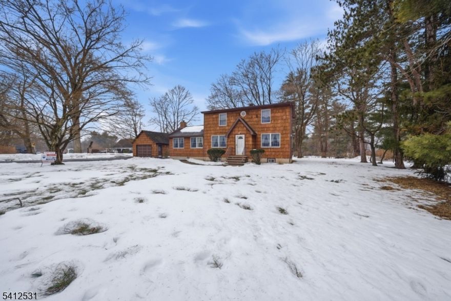 Welcome to this beautifully maintained Colonial set on just under one acre of park-like land, ideally positioned on a quiet corner lot. Offering five bedrooms and two full baths, this spacious home provides a flexible layout perfect for today's lifestyle. Four bedrooms are located on the second floor, with an additional bedroom conveniently situated on the main level. The first floor features a formal dining room, living room, and a spacious eat-in kitchen complete with stainless steel appliances. The expansive family room is the true centerpiece, boasting vaulted ceilings, skylights, a wood-burning fireplace, and doors that open to a large deck overlooking the rear portion of the property perfect for entertaining or relaxing outdoors. Hardwood floors and abundant natural sunlight enhance the warmth and charm throughout the home. The basement offers excellent potential with the added convenience of a Bilco door for easy access. Additional highlights include a detached one-car garage and ample parking. Ideally located near major highways, parks, restaurants, and shopping, this home is also situated within the highly regarded Mount Olive Township School District.