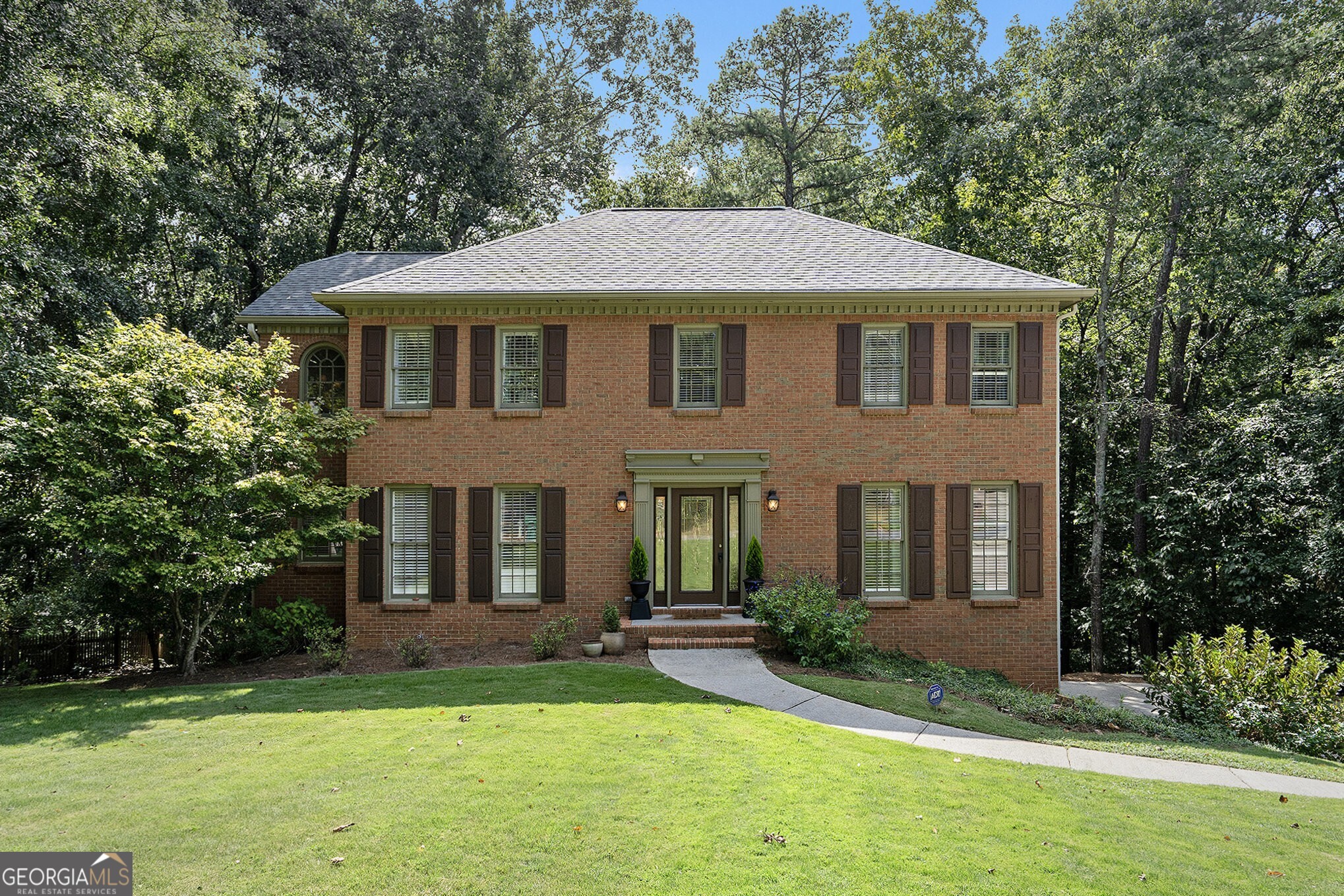 Traditional Brick Beauty in Bentley Place near Berkeley Lake in Peachtree Corners! Welcome to this charming Brick Home tucked on over half an acre in the tranquil and established Bentley Place neighborhood. From the moment you arrive, the Curb Appeal is Impeccable with a Large Grassy Front Yard, timeless brick fa ade, dark shutters, and a welcoming entry framed by mature trees and lush landscaping. Step inside to be greeted by Dark Hardwood Floors, Crown Molding, and a spacious entrance Foyer. To your left, a Formal Dining Room sets the stage for hosting and memory-making, leading seamlessly into the Chef's Kitchen complete with Granite Countertops, White Cabinets with open shelving, Stainless Steel Appliances, and a Breakfast Nook Wrapped in Windows with peaceful views of the Backyard. The heart of the home is the Fireside Family Room, featuring an Elegant White Mantel and Custom Built-Ins. The main level also offers a dedicated Home Office or Flex Space, Laundry Room, and convenient Powder Room. Upstairs, retreat to the expansive Primary Suite with a Walk-In Closet and En-Suite Bathroom boasting a Soaking Tub, Double Vanity, and separate Glass Shower. Three Additional Bedrooms share an updated Full Bath with a stone vanity and stylish tile finishes. The Daylight Terrace Level provides Two Versatile Bonus Spaces perfect for a Gym, Playroom, Media Room, or Second Office. Outdoors, a Spacious Deck overlooks the large, private backyard with a balance of wooded privacy and grassy play areas, ideal for relaxation or entertaining. Shaded by mature hickory trees, the backyard offers seasonal nut harvests and a beautiful natural backdrop featuring hummingbirds, deer, turtles, squirrels, and chipmunks. A Two-Car Garage completes this wonderful home. Located in the sought-after Berkeley Lake Elementary district, just minutes from The Forum on Peachtree Parkway, Golf, the Chattahoochee, and quick access to I-285 and I-85, this home blends Classic Charm with Modern Convenience in a serene yet accessible location.