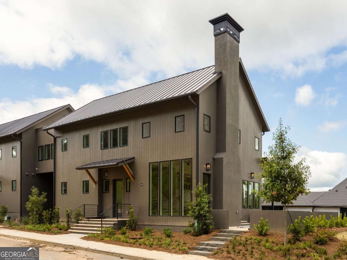 Perched on peaceful Lupo Loop, this beautifully designed home offers open-concept living with a soaring two-story living room bathed in natural light. The main level includes a private primary suite and flows effortlessly to ample outdoor space-including a large entertaining patio, side yard, and a back porch with stunning treetop views. The terrace level features an additional yard space, perfect for a garden or future pool. Upstairs, two guest bedrooms with en-suite bathrooms and a cozy loft create the perfect retreat for guests or a quiet home office. ? This home is ideally situated across from the Lupo Loop Ridgeline nature trail, giving you access to the Grange Hamlet from a short distance and while also being centrally located just above the Mado Hamlet for access to all of Serenbe's renowned wellness amenities. With direct access to over 20 miles of soft-surfaced nature trails and generous outdoor living spaces, this home truly blends nature, comfort, and convenience.