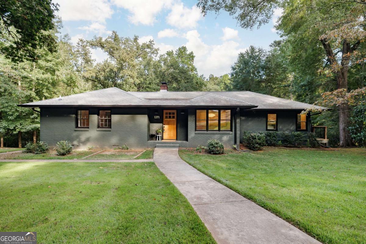 Set on 1.76 acres at 1391 Ivywood Dr in Oconee County's Ivywood subdivision, this all-brick ranch offers single-level living with the convenience of an Athens address. It balances privacy and accessibility. Hardwood floors run throughout. The kitchen features original cabinetry, stainless steel appliances, butcher block counters, and a pantry, with space for casual dining or a keeping area. The main living area features a wall of windows and connects to flexible spaces, including a home office/den and a sunlit laundry room. Three bedrooms and two full baths, including a private suite, complete the main floor; both baths were renovated in 2022. The finished basement offers a one-bedroom apartment with kitchen, living area, bath, and private entrances-renovated in 2022 and ideal for guests, family, or income potential. Outdoors are mature trees, a creek, and a detached two-car garage with electrical and plumbing, perfect for a workshop or expansion.