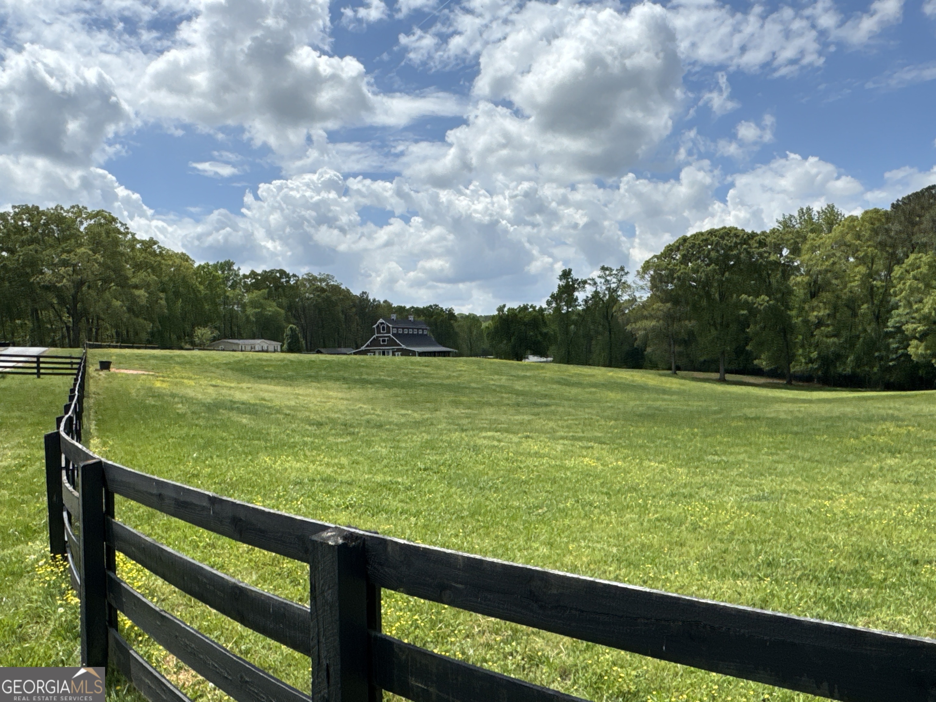 Welcome to a truly exceptional equestrian estate, gracefully set on 50 rolling acres in southeastern Cherokee County-just minutes from Milton and Hwy 20. Blending natural beauty with sophisticated design, this rare offering boasts a picturesque landscape of open pastures, mature woodlands, and serene frontage along Canton Creek, offering the perfect balance of privacy, prestige, and convenience. At the heart of the property lies a breathtaking 18-stall, custom post and beam barn, a showcase of craftsmanship and equestrian luxury. The barn features 12 thoughtfully designed exterior 12'x12' stalls and six oversized 12'x16' tongue-and-groove interior stalls, one of which is an expandable foaling stall. Accented by two elegant chandeliers, the barn also includes dual tack rooms, a feed room, a wash area, and a full bathroom with washer/dryer hookups and dedicated hot water. A spacious loft provides abundant storage, and a new roof was installed in April 2025. Exterior amenities include additional wash racks, a separate hot water heater, and hookups for fans and lighting-ensuring comfort and efficiency year-round. The estate also offers both a covered arena and an outdoor riding arena, each fully lit and professionally maintained with M10 and river sand footing. Included are all jumps, dressage mirrors, mounting blocks, and rail systems. Black, four-board fencing surrounds the grounds, which include multiple turnout paddocks, established cross-country trails, and additional jumps throughout the lower pasture. Additional improvements include a hay shed, barn manager's lodging (with a new roof as of April 2025), and a gated entrance with keypad access. The septic system was fully serviced in February 2025. Previously operating as The Stables at Union Hill, this refined equestrian property presents a rare opportunity to own a turnkey facility with room to expand or personalize. Whether you're looking to train, board, or build a luxury estate residence, this property offers an unmatched setting in one of North Georgia's most coveted equestrian corridors.