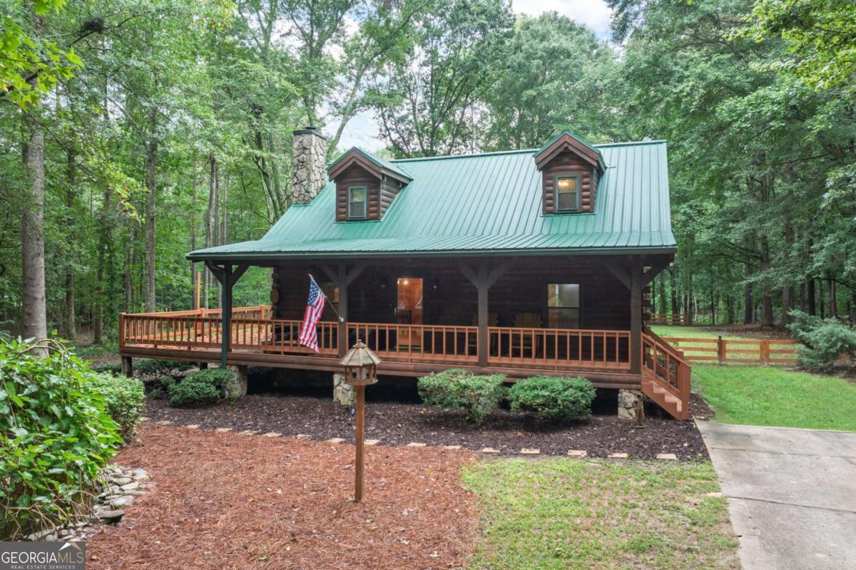 Privacy on almost ten acres. Endless possibilities. Down a private drive, this handcrafted log cabin rests among whispering pines, its wide front porch overlooking a koi pond and gentle stream. Inside, soaring wood-beamed ceilings frame a stone fireplace with a wood stove, while the kitchen blends rustic style with modern convenience-featuring custom cabinetry, granite counters, and stainless appliances. A main-level bedroom, full bath, and laundry add ease; upstairs offers a spacious suite, a loft, and another full bath. Outside, explore winding trails, shady picnic spots, and a deck made for gathering. Adding tremendous value are multiple workshops with power and storage buildings that stand ready for projects or gear. And yes, there's a skid steer and bobcat on the property. The story's even better in person.