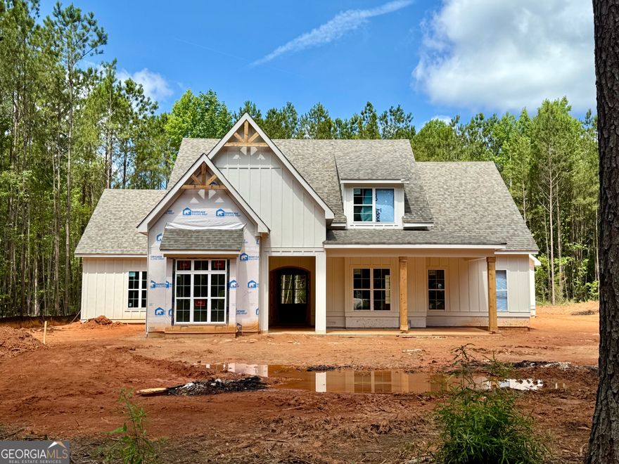 Set on a picturesque 3-acre lot in one of the area's most coveted locations-with effortless access to Peachtree City, Newnan, and Senoia-this stunning custom home is a masterfully enhanced version of Mitch Ginn's celebrated Elberton Plan. Every square foot has been intentionally designed with livability, luxury, and lasting quality in mind. From the moment you enter, you'll feel the harmony between style and function. At the heart of the open-concept layout lies a chef-inspired kitchen-anchored by a generous island with seating, custom cabinetry, quartz countertops, and a walk-in pantry with beautifully crafted shelving. The kitchen flows effortlessly into the dining space and fireside living room, where a 10-foot sliding glass door invites you out to the oversized, covered rear porch. With flagstone flooring, a fireplace, tongue and groove ceiling, and views of your private acreage. Inside, the home offers five spacious bedrooms, four of which are on the main, each with a private en-suite bath and walk-in closet. The primary suite is a retreat of its own with his-and-her custom closets, dual vanities, a freestanding soaking tub, and a beautifully tiled shower. A convenient half bath is perfectly placed for guests and easy access from the porch.  The second floor offers even more flexibility with a private guest or teen suite-complete with its own full bath and walk-in closet.  Additional highlights include hardwood flooring throughout, tiled wet areas, spray foam insulation, tankless water heater, a spacious laundry room off the kitchen and garage, and a three-car garage. Four sides  irrigation, energy-efficient systems, and elegant finishes round out this thoughtfully built home. A rare opportunity to own a refined, functional home in a setting that feels both tucked away and totally connected. Pop in and see the progress as the final touches are completed-this is a home you'll want to experience in person.