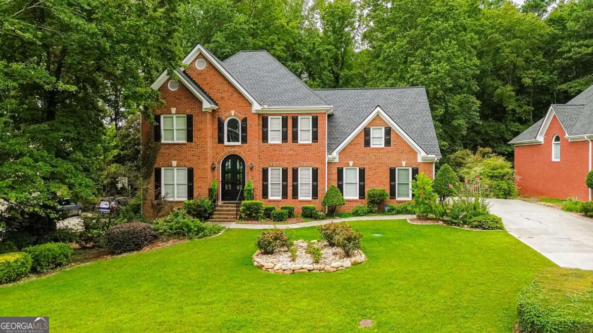 Behind its timeless brick facade and double arched doors, this Lakes of Old Peachtree home delivers style, space, and sophistication in the sought-after Mountain View HS district. A sunlit foyer opens to a fireside family room with soaring ceilings and picture windows, flowing into a sleek white kitchen with stainless appliances, stone counters, gas cooktop, and double ovens. Upstairs, the primary suite impresses with a tray ceiling, sitting area, spa bath, and boutique-style closet, joined by four additional bedrooms. The finished terrace level is built for entertaining with a full bar, media/game lounge, theater room, fitness space, and walk-out access to the backyard. Outdoor living shines with an oversized deck, covered patio, and deep, level lawn framed by mature trees and blooming roses. With a like-new roof (2022) and access to swim/tennis amenities, this move-in ready home offers a perfect blend of elegance, comfort, and convenience-minutes to Mall of Georgia, I-85, and Hwy 124.