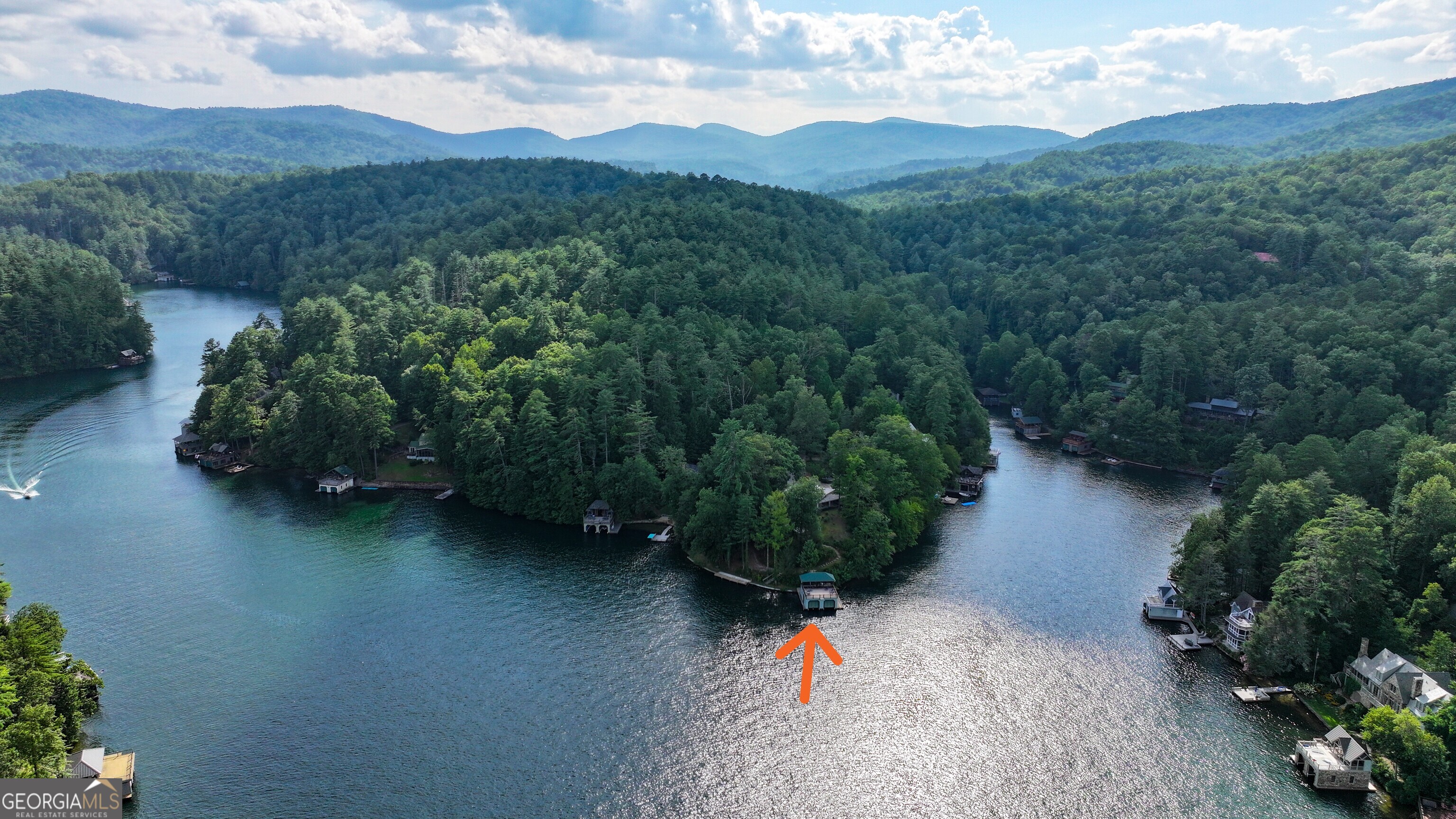 A RARE LAKE RABUN ESTATE Own a remarkable piece of Lake Rabun's history with this extraordinary 1.36-acre lakefront property. Tucked away at the end of a private road, this one-of-a-kind estate boasts MORE THAN 406 FEET OF LAKEFRONT SHORELINE WRAPPING AROUND A DEEP-WATER PENNINSULA in one of the lake's largest basins. The original mid-century U-shaped brick ranch, designed and built in the late 1960s with local materials and craftsmanship, welcomes you with a stone-paved courtyard and enchanting raised rock garden. Inside, vaulted wood-beamed ceilings, locally milled paneling, handcrafted shelving, and a massive mountain-stone fireplace create timeless warmth. Walls of windows and oversized sliding doors capture sweeping panoramic lake views, opening to a covered wraparound patio with multiple seating areas. The kitchen-highlighted by its own brick-front cooking fireplace, handcrafted cabinetry with leaded glass, and expansive prep space-overlooks the lake. Accommodations include a main-level master suite with dressing room, a private-entry guest suite with lakeview deck, and a spacious one-bedroom terrace-level apartment with full kitchen, living room with fireplace, and walk-out patio. Additional spaces include a two-car carport with full bath and deck (designed for easy guest suite conversion) and a large heated workshop with water and electricity. Stone steps lead to the shoreline, where a 2010 double-decker, two-slip boat dock with lifts awaits. The upper level offers both screened and open sections with ceiling fans, TV mount, sun deck, and jump platform. The property also retains its original swim dock with rock steps into the lake. Georgia Power has previously approved plans for possible expansion of lake-level decking and swim docks, creating opportunity for even larger gatherings. Lovingly cared for through the decades, this property offers a rare combination of privacy, unmatched shoreline, and breathtaking views. Whether you choose to restore its mid-century character, update with modern luxury, or design a brand-new lakefront retreat, this estate represents an extraordinary opportunity on Lake Rabun. Known for its crystal-clear waters, majestic mountain backdrop, and warm, close-knit community, Lake Rabun is the perfect setting for a truly remarkable lakefront lifestyle. Agent is part owner.