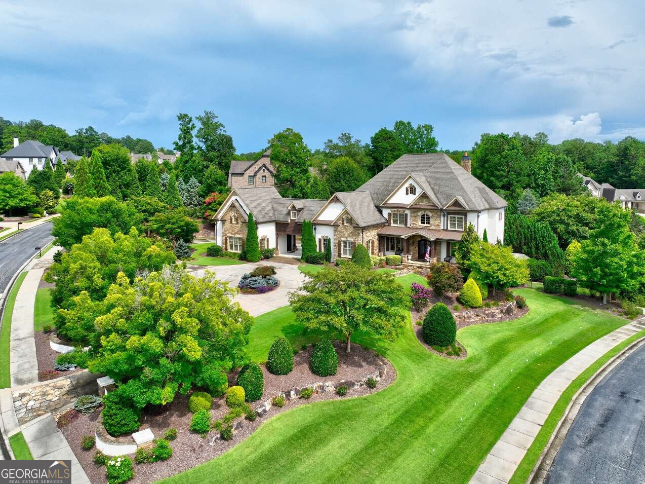 Welcome to Luxury Living in the Heart of Milton! Located in the prestigious, guard-gated Manor Golf & Country Club, this custom-built estate offers over ~9,000 sq ft of heated/cooled living space on a beautifully terraced 1.19-acre corner lot with views of the Tom Watson Championship Golf Course. This 6-bed, 7 full bath & 2 1/2 bath home is designed for entertaining and comfort, featuring 10-ft ceilings, custom crown molding, floating staircase, and abundant natural light throughout. The expansive main level includes a gourmet kitchen with Wolf & Sub-Zero appliances, oversized island, double sinks, pot filler, warming drawer, and dual Asko dishwashers. Enjoy an adjacent walk-in pantry with rolling ladder, command center desk, and mudroom with 2nd laundry. The open floor plan flows into a stunning keeping room with vaulted ceiling, Palladian window, and stone fireplace. A formal dining room and wet bar with wine cooler make entertaining easy. The guest suite on main includes a large ensuite bath and tray ceiling. Step outside to a resort-style backyard with covered patio, outdoor kitchen (Viking grill, side burner, fridge), wood-burning fireplace, pool with hot tub & sun ledge, firepit, and lush seating areas. Professionally landscaped by Cartwright Landscapes, the backyard also features 350+ linear ft of custom stone walls. Upstairs, the primary suite features a triple tray ceiling, fireplace, spa bath with double showers, rain head, large bench, and a custom dressing room with 8' vanity. A breezeway leads to the private executive office suite above garage bays 4 & 5, with vaulted ceiling and private access for early departures or late returns. Three additional upstairs suites offer walk-in closets and private baths, plus a large bonus room with built-in desks, storage, and tech space. Main laundry is also upstairs. The finished terrace level includes a full kitchen with large island, full fridge/freezer, icemaker, microwave, range, and dishwasher. Enjoy a large den, game area, media room (10 seats, 86" Sony TV), gym with rubber flooring and steam shower, private bedroom with full bath, and workshop/craft area. Tech closet is fully wired for smart home integration, with network, audio, video, and coax pre-wired throughout. 5 garage bays, circular drive, and extended parking behind the portal garage make hosting easy. Community amenities include: 24-hour security, clubhouse, fitness center, restaurant, indoor/outdoor pools & tennis (hardcourt & clay), sidewalks, and world-class golf. Close to top-rated schools, Hwy 400, and shopping/dining in Milton, Alpharetta, Halcyon, and Avalon.