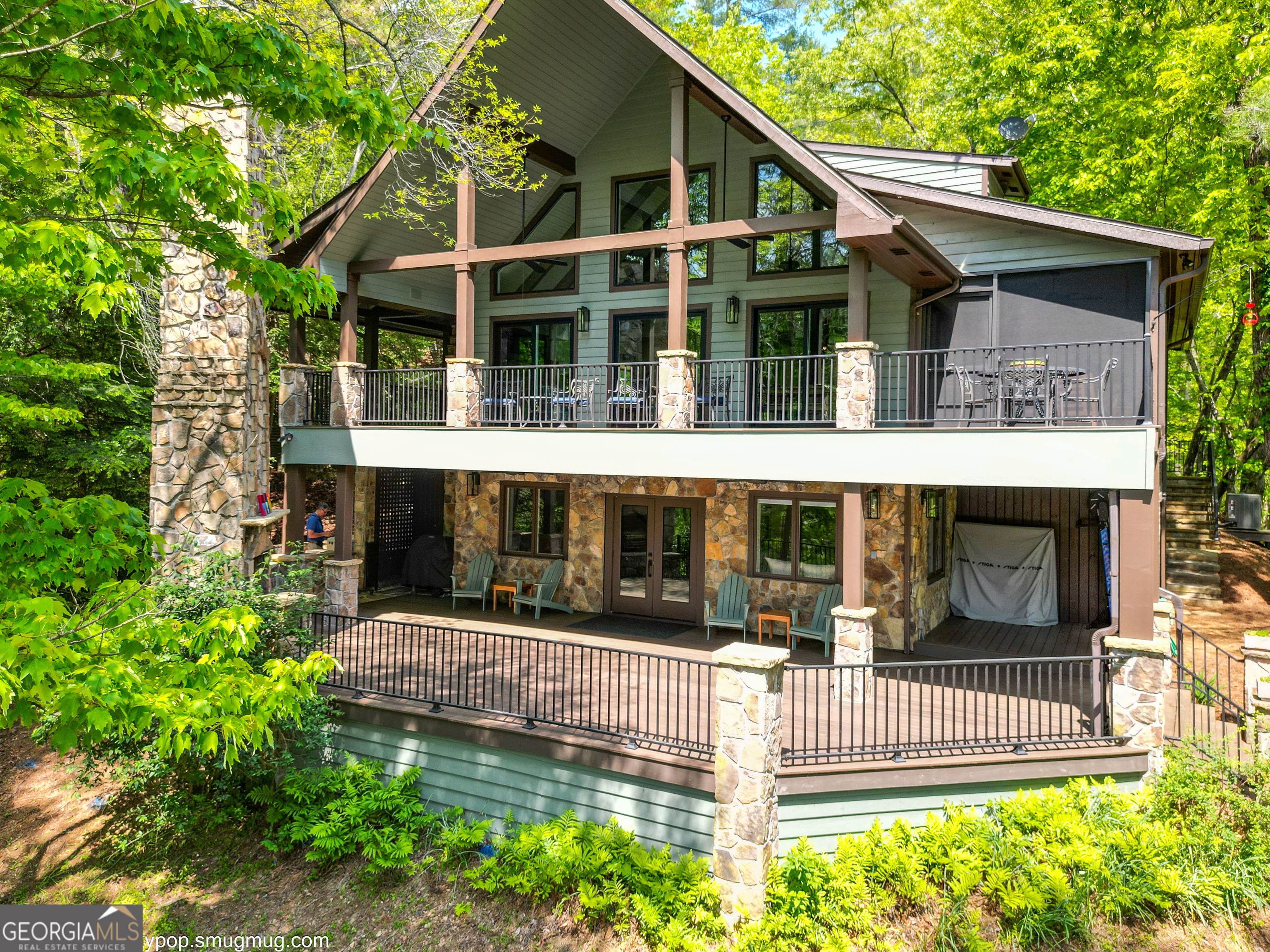 This breathtaking lakeside sanctuary features an exquisitely designed layout that spans multiple levels seamlessly blending luxury with comfort. The concrete driveway and spacious parking pad leads to a delightful cottage garden adding a charming natural touch to the property. The covered front porch offers a warm welcome to all who arrive. Upon entering, a floating staircase, adorned with a sleek wire railing that adds a contemporary touch to the home's sophisticated design, leads from the main level to the loft. At the loft level, you'll find a spacious bedroom complete with a large closet, extra attic storage space, and a full bathroom featuring a stunning all-tile shower and marble vanity counter top. The loft also includes a dedicated study area, equipped with elegant built-in cabinetry. Natural light floods through new windows and glass doors in both the kitchen and the great room, providing captivating views of the lake from the main level. The main floor is a culinary dream, showcasing a dining room and a gourmet kitchen equipped with the latest appliances from late 2023. The kitchen features custom storage solutions that maximize space and functionality. Luxurious quartzite countertops are complemented by a striking island with a graceful quartzite waterfall. The great room exudes elegance boasting vaulted ceilings and a cozy stone fireplace that invites relaxation. Adjacent to the main living area is a chic custom half bath featuring quartzite countertops that match the high-end finishes found throughout the home. The opulent master suite features a lavish bathroom outfitted with dual sinks, a private water closet, an all-tile shower, matching vanity quartzite countertops, custom cabinetry, and ample storage. Step out onto the screened porch, featuring an invisible screen system and ceiling fan, which leads to a wrap-around deck with picturesque lake views. This deck with iron rails and TimberTech decking is ideal for entertaining guests and enjoying morning coffee. The versatile terrace level expands your living space and features a mini kitchen and a convenient wet bar, along with another inviting stone fireplace. This level also includes two spacious bedrooms, one of which is a unique bunkroom fitted with two x-long custom oak beds designed and built by an Asheville Craftsman. The full bath features custom granite countertops, a tile shower, a water closet, and custom cabinetry. The utility room boasts a new heating and cooling system (installed in 2023), a washer and dryer with a utility sink, a water filtration system, a tankless water heater, a freezer/refrigerator and more custom storage. All levels of the house have zoned air conditioning with individual thermostats. The thoughtful addition of a mud room, tool storage area with a roll-up door and stone steps connecting to the parking pad facilitate rainy day house entry, tool and bear proof garbage storage. Outside, you'll discover a sprawling terrace-level deck with unobstructed views of the glimmering lake, complete with a grand stone fireplace ideal for memorable gatherings. Additional highlights of this remarkable property include a powerful 24KW Generac generator housed in a beautifully crafted stone enclosure. This home is designed for low maintenance, featuring TimberTech decking and elegant black iron railings throughout the majority of the exterior areas, along with stone pathways and stairs that lead from the house to an impressive two-slip boathouse built (2016). The boathouse features an upper TimberTech deck with iron railing, ceiling fans, lighting, and a mini refrigerator for your convenience. This home epitomizes elegance and low-maintenance living, representing luxurious lakeside living at its finest.