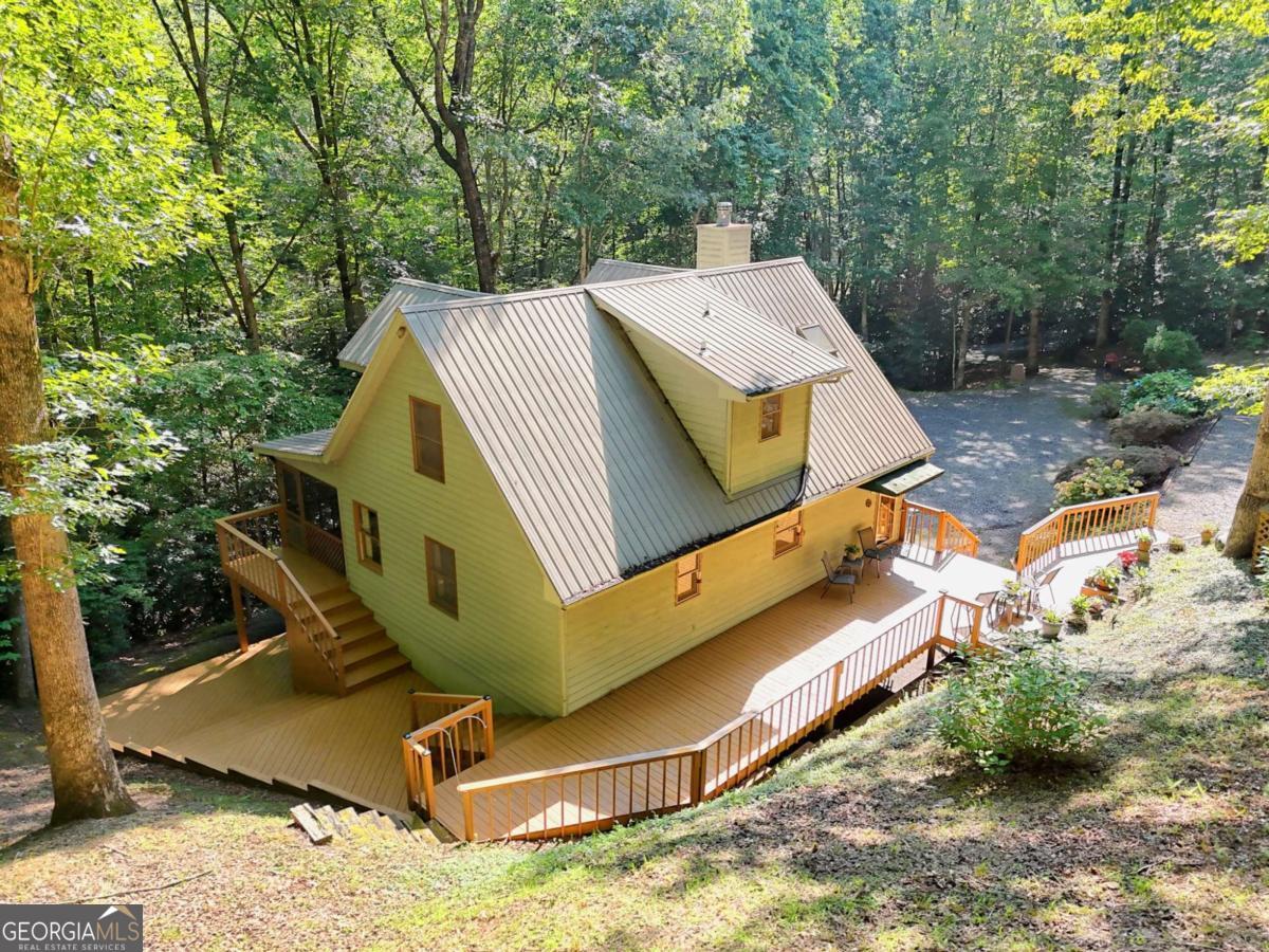 Located on 3.28 acres, this beautifully maintained homestead perfectly balances tranquil seclusion with convenient access to the local fare of Hiawassee, being minutes away. Step inside to experience a true cabin ambiance, featuring wood walls and a cathedral ceiling, a floor-to-ceiling stone fireplace, an open dining area and kitchen, and stairs leading to a loft. The kitchen features beautiful light shiplap ceilings, maple cabinetry, and stainless steel appliances. Adjacent to the kitchen is the Primary Suite, featuring an updated seamless glass shower, a walk-in closet, and private access to the screened porch that overlooks a wooded backdrop. Venture upstairs to find a charming sleeping loft and a private guest suite with an updated bath. The lower level is equally impressive with a bedroom with a full bath, flex room, practical laundry facilities in the utility room. Plus, a workshop area with garage door access for your ATV adds convenience to your outdoor lifestyle, in addition to a covered patio that leads to a lower-level open-air deck. Two driveways optimize access-one leads to a welcoming open-air deck and the main level, while the other navigates directly to the lower level. The beautifully landscaped grounds, adorned with rock walls and native plants, require minimal upkeep. Naturally, mountain property becomes more appealing when complemented by a peaceful creek to enjoy. With a carport and handy storage outbuilding, this property has everything you need to embrace a quiet lifestyle in this exceptional mountain haven!