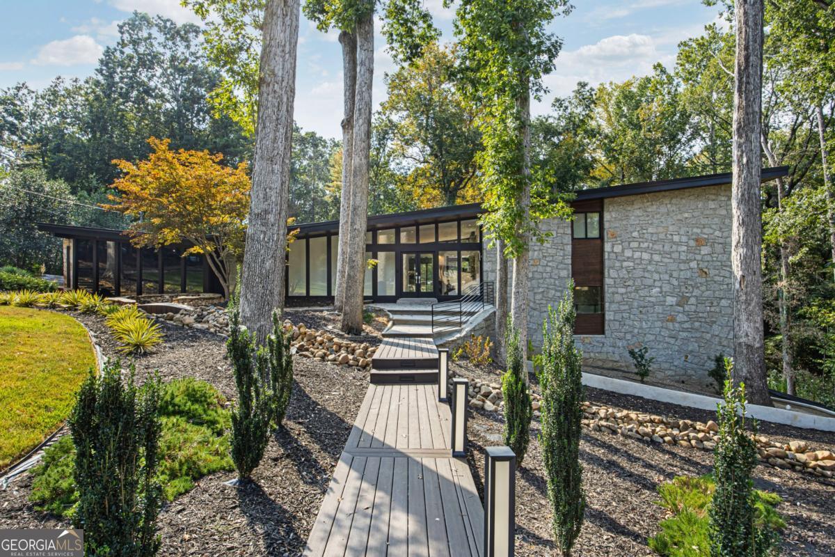 Welcome to 4144 Flintlock Road NW, a fully renovated mid-century modern masterpiece in the heart of Buckhead. Set on a private 1.24-acre wooded lot, this home offers over 5,500 square feet of luxurious living with an open, light-filled layout. Floor-to-ceiling windows, hardwood floors throughout, and a dramatic great room create a seamless flow between sophisticated gathering spaces. The chef's kitchen features custom cabinetry, professional-grade appliances, and a walk-in pantry, while the sunken den leads to a unique secondary owner's suite with two attached bathrooms. The primary suite is a true retreat, highlighted by a spa-like bath with dual vanities, soaking tub, and oversized shower. Designed for both relaxation and entertaining, the finished basement level is designed for entertainment and wellness which boasts a fully equipped second kitchen and a private gym. Don't forget beautiful home theater with wet bar! Outdoor living is equally impressive with expansive decks, lush landscaping, and a serene koi pond. With multiple owner's suites, versatile living areas, and thoughtful modern upgrades-including smart home features-this property balances elegance and functionality. Located in the prestigious Mount Paran-Northside community and zoned for top-rated schools, it is a rare opportunity to enjoy privacy, luxury, and convenience in one of Atlanta's most sought-after neighborhoods. Surrounded by homes selling at $2.5M and above, this residence is offered at an incredible $1,895,000, presenting a rare opportunity to enjoy privacy, luxury, and value in one of Atlanta's most sought-after neighborhoods. Please note: All showings require re-approval prior to confirmation.