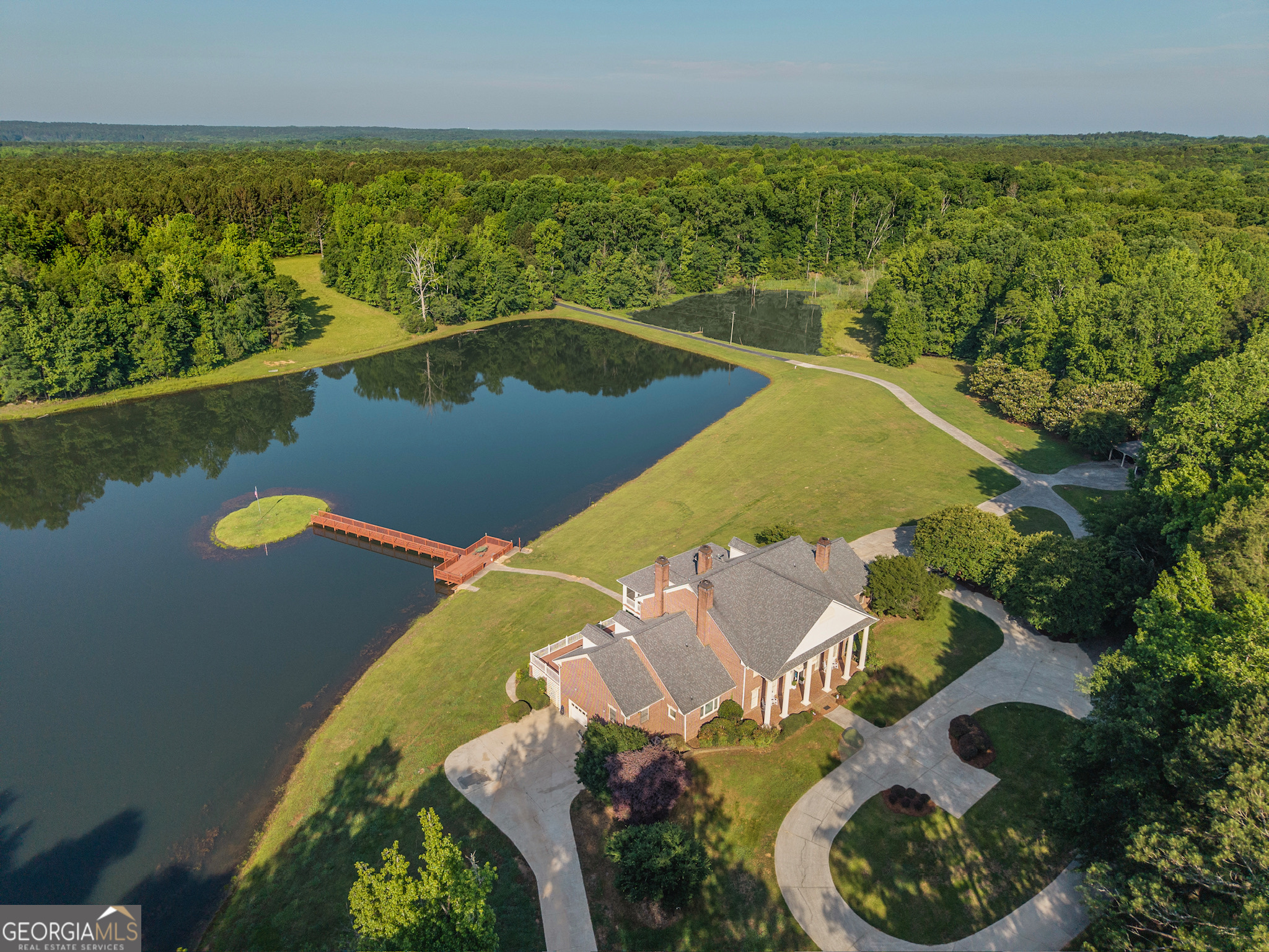 Welcome to Scarlett Oaks - an extraordinary 1,028-acre legacy property that represents the pinnacle of recreational southern living. A rare and irreplaceable assemblage more than 40 years in the making, this iconic estate features more than 2 miles of frontage on Doster Road, one of Madison's most treasured country roads, and 1.5 miles on scenic Double Bridges Road. Gated entrances on both road frontages, and winding paved drives leading past mature trees and a creek bed, set the stage for an elegant arrival. At the heart of the property lies an 8 acre private lake and a breathtaking 10,000+ square-foot estate home. Perfectly positioned to capture sweeping water views from expansive patios and wide veranda's, the stately residence reflects the gracious style of a true southern estate. The home features a marble-floored foyer with sweeping staircase, formal living and dining rooms with fireplaces, a lakeside kitchen and informal dining room, and a richly paneled study with built-ins and a wet bar. Nearly every rear facing room in the home opens to an expansive veranda or patio overlooking the lake - seamlessly blending indoor and outdoor living. The main-level primary suite is a peaceful lakeside retreat, complete with a fireplace, private patio access, and luxurious dressing rooms and closets. Upstairs, five en-suite bedrooms surround a dramatic, vaulted trophy room. An additional laundry room and storage rooms, a discreet back staircase to the kitchen, and a Juliet balcony overlooking the circular drive round out the features on this level. On the lower level, you'll find a full guest or caretaker suite with private kitchen and living area, as well as a recreation room with a pool table, many storage and utility rooms, and an additional 4-car garage. A private elevator connects all levels, and a full-sized attic - already stubbed for future bedrooms and baths - offers room to grow. The estate also includes a detached office building with a half bath, ideal for managing land operations or working remotely. Throughout the 1,028 acres you'll find miles of trails, flowing creeks, mature hardwoods, open fields, and well-placed food plots-making it a haven for hunting, exploration, and outdoor enjoyment. For those seeking an even grander footprint, two additional tracts - a directly adjoining 174 acres with a lodge-style residence, and another 150 acres on Double Bridges Road-are also available, offering the potential to control more than 1,350 acres in one of Georgia's most beautiful rural corridors. Located minutes from historic downtown Madison and within Georgia's renowned Lake Country, Scarlett Oaks is surrounded by natural beauty, small-town charm, and a thriving outdoor culture. This is more than just a property. It's a once-in-a-generation opportunity to own one of Georgia's most significant private estates.