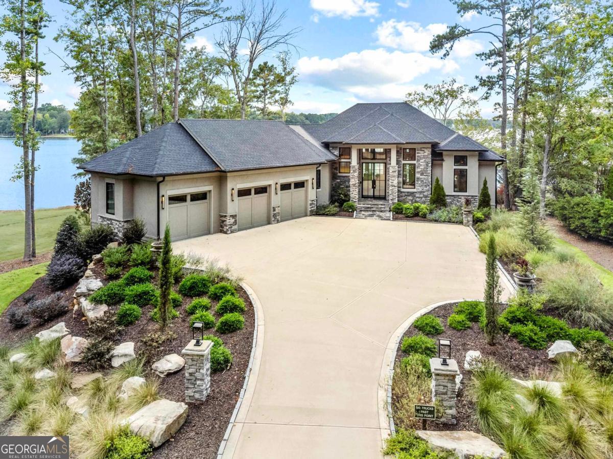 Luxury Lakefront like-new custom home with all the amenities in Reynolds Lake Oconee showcasing the most breathtaking, expansive lakeviews imaginable. Nestled on nearly an acre of lakefront, this stunning home offers modern elegance with high-end finishes throughout. The long private driveway sets the tone for the grand experience that awaits inside.The 24-ft ceiling great room with 9-ft glass sliders seamlessly invite the outdoors in offering front-row sunset views. Designed with style and convenience in mind, this smart home delivers a sophisticated yet welcoming ambiance.The custom cast iron front door opens to a striking interior with custom Italian tile flooring, designer lighting, floating iron and wood staircase highlighted by a custom antique mirrored glass, remote-controlled electric fireplace. The exceptional open floorplan was designed to capture views of the lake from nearly every room. The kitchen is framed by Bentley cambria quartz waterfall countertop island and coordinating vent hood, sleek custom cabinetry, and professional designer appliance package that include Sub-Zero refrigerator, Wolf cooktop, Cafe Professional Series oven, Cove dishwasher, ice maker, dual refrigerator drawers, and a 288-bottle Zephyr wine refrigerator. The luxurious primary suite boasts 10" natural hardwood plank floors, remote-controlled electric fireplace, custom Artisan closets, and a  spa-like bath with floor-to-ceiling tile throughout, natural wood vanities and cabinets with concrete vessel sinks. The main level also include a versatile office that can easily serve as an additional bedroom. A beautiful floating iron staircase leads to the terrace level where a spacious family room and billiard room await. This level is an entertainer's dream featuring a full bar, powder room and a seamless access to the pool deck with expansive lake views as the perfect backdrop. The rare flat lake backyard is a true gem in this community.The terrace level also features three well-appointed guest suites ensuring ample space for family and friends. Watch your favorite games in your expansive outdoor deck or enjoy the sunset in your salt water pool/spa with spillway, automatic cover and fire pit. This luxurious home features remote control blinds, three-car garage,large custom seasonal closet and Smart Home features (security, pool,firepit,lighting).Location is unparalleled. Walk to the clubhouse and the Jack Nicklaus course.  Membership is available.