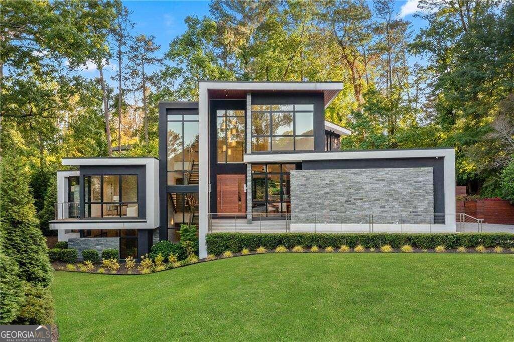One of Atlanta's truly most iconic modern residences, 1345 Navajo represents the pinnacle of architectural innovation, designed and built by the acclaimed design studio, FLUX modern. Boasting five bedrooms and six and a half bathrooms, Navajo Residence seamlessly integrates indoor/outdoor living across its nearly 6000 sqft of living space. Navajo Residence is stately poised atop a natural ridge above the quiet Brookhaven cul-de-sac it calls home. A highly curated palette of exterior materials blend seamlessly as smooth polished hardcoat stucco, western red cedar wood, and southeastern Asian slate stones are harmoniously blended together to be in sync with the home's natural surroundings. You are welcomed home by a massive 10' pivot front door and are drawn into the heart of the home by a soaring double-height foyer and great room. A massive floating stairwell connects the three distinct levels of living space. The natural stone wall flows from the exterior faoade inside highlighting the indoor/outdoor nature of this home. A massive wall of glass completely pockets open continuing the experience all the way through the home to the exterior anchored by an incredible lap pool with a signature stone waterwall feature. The living room is anchored by a dramatic 6' linear stone fireplace and custom built-ins. Site-finished oak flooring seamlessly flows throughout the main level, tying Navajo Residence's living spaces. Floor-to-ceiling Cantina window and door systems offer the highest level of energy-efficient glazing technology, and in spectacular fashion allow entire walls of glass to effortlessly slide open while flooding the home with natural lighting during all seasons. FLUX has become a standout in the modern home space with an emphasis on modern designs with both a high level of aesthetic appeal while combining the latest in technology while affording functionality and practicality. This is no more evident than in the massive kitchen with its floor-to-ceiling dual-tone custom flat-panel cabinetry, 3" thick quartzite counters, ultra-high-end appliance package all set against a massive Monte Blanc quartize slab backsplash. A main-level Owner's Suite is a true respite affording an unparalleled space for rest and relaxation. With truly panoramic views of the ultra-private yard and resort-style pool. Double floating vanities, floor-to-ceiling marble tile, a massive double walk-in shower and a freestanding soaking tub centered on a picture window with serene views make for an idyllic owner's bath experience. On the main floor, the dining room, guest bedroom, powder room, living room, laundry, and pool bathroom round out the main living level. Each area offers either picturesque views or direct access to the rear patio, blurring the distinction between inside and out. Step onto the rear lanai, a sanctuary of relaxation and entertainment. Here, the resort-style pool and patio beckon, framed by three exquisite fossilized stones amidst the tranquil water feature. It's a haven for large-scale entertaining or quiet al fresco moments alike. Luxury abounds within, with high-end finishes, appliances, and fixtures elevating every corner of the home creating a living experience that transcends boundaries and redefines modern luxury living. Nestled in the Murphy Candler Park neighborhood, residents enjoy unparalleled access to recreational amenities, including parks, athletic fields, trails, and tennis facilities. Plus, its central location offers easy commutes to Perimeter Mall, 285, Medical Center, Brookhaven restaurants, Sandy Springs, and Buckhead, ensuring convenience without compromise.