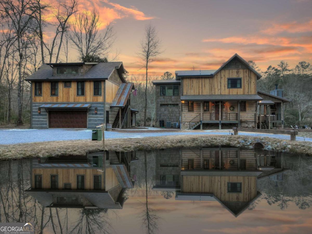 Welcome to the Toccoa Tailwater Fish Camp, a newly built 2024 lodge-style retreat offering over 300 feet of private Toccoa River frontage with a stocked pond on 6 acres. This one-of-a-kind property combines rustic craftsmanship with luxury finishes, designed for the ultimate fly-fishing and mountain lifestyle experience. The main lodge features 4 bedrooms, 3.5 baths, with 3 bedrooms facing the river, each with its own electric fireplace. Vaulted ceilings, cedar beams, chink-style siding, and designer fixtures enhance the warm lodge feel. Expansive windows frame river views while the chef's kitchen boasts granite countertops, custom cabinetry, and high-end appliances. The spacious party porch with a stone fireplace creates the perfect place to entertain while overlooking the river's natural rock shoals and waterfalls. The guest house, located above the 2-car garage, provides a private retreat with a living room, kitchen, 2 bedrooms joined by a bath, plus a loft for extra sleeping. A cozy covered porch with its own fireplace also faces the river, offering privacy and charm. Below, the custom speakeasy room is ideal for cocktails, games, or gatherings. Outdoors, a private stocked pond in the front yard is perfect for practicing your cast, while stone steps lead directly into the river to reach prime fishing holes. The gated entrance welcomes you into this fisherman's paradise, complete with thoughtful touches, true cedar log beams, and lodge-style details throughout. An additional buildable lot is included, featuring a 2-bedroom septic and power already in place-ideal for expansion or investment. Whether you're a serious angler, nature enthusiast, or seeking a luxury mountain escape, this property delivers an unmatched opportunity to own your private lodge on the Toccoa River.