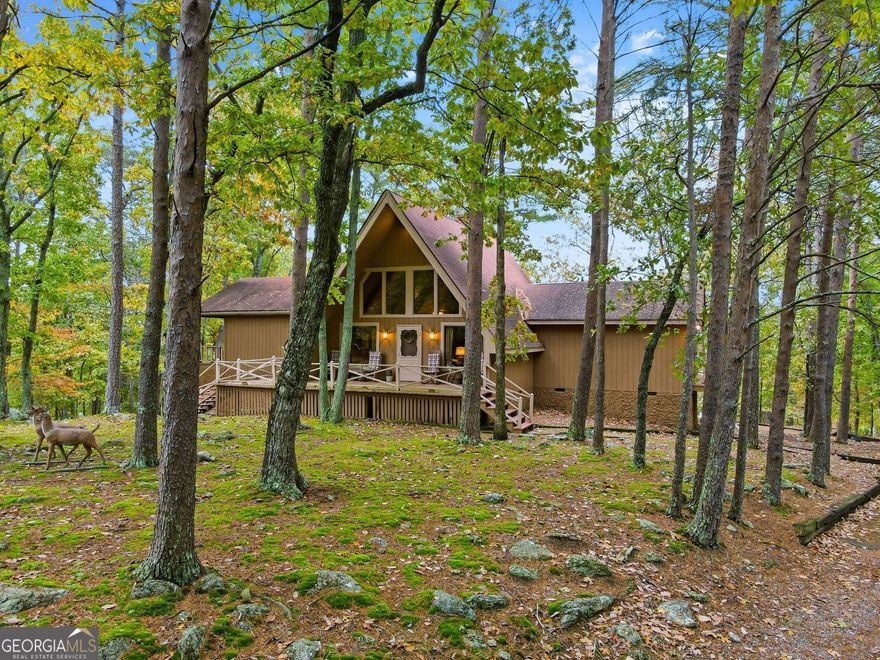 Tucked into the trees in sought-after Lake Arrowhead, this chalet-style home offers rustic charm and room to grow. The main floor opens with a striking vaulted living area, where warm, tongue-and-groove ceilings soar above a stone fireplace, center stage for cozy nights or casual gatherings. A wall of windows fills the space with natural light, while the open layout connects seamlessly to the dining area and vintage-style kitchen. Painted cabinetry, wrap-around countertops, and access to the deck make this kitchen both functional and full of character. Just off the living room, the primary bedroom features an ensuite bathroom and access to a covered deck. Two additional bedrooms on the opposite side of the house offer flexibility for guests or workspace, and another full bathroom is conveniently located just down the hall. The unfinished walkout basement offers an opportunity to customize, whether you're dreaming of a media room, workshop, or gym. There are already two small closets in place for extra storage, as well as a third full-size, unfinished closet space. Outside, enjoy a large front & back deck with peaceful treetop views, a covered carport with access to the front entry, and a low-maintenance wooded lot that feels like a mountain retreat. All of this within a gated, amenity-rich community featuring golf, swimming, tennis, dining, and miles of hiking trails, plus one of Georgia's cleanest lakes just minutes from your door.