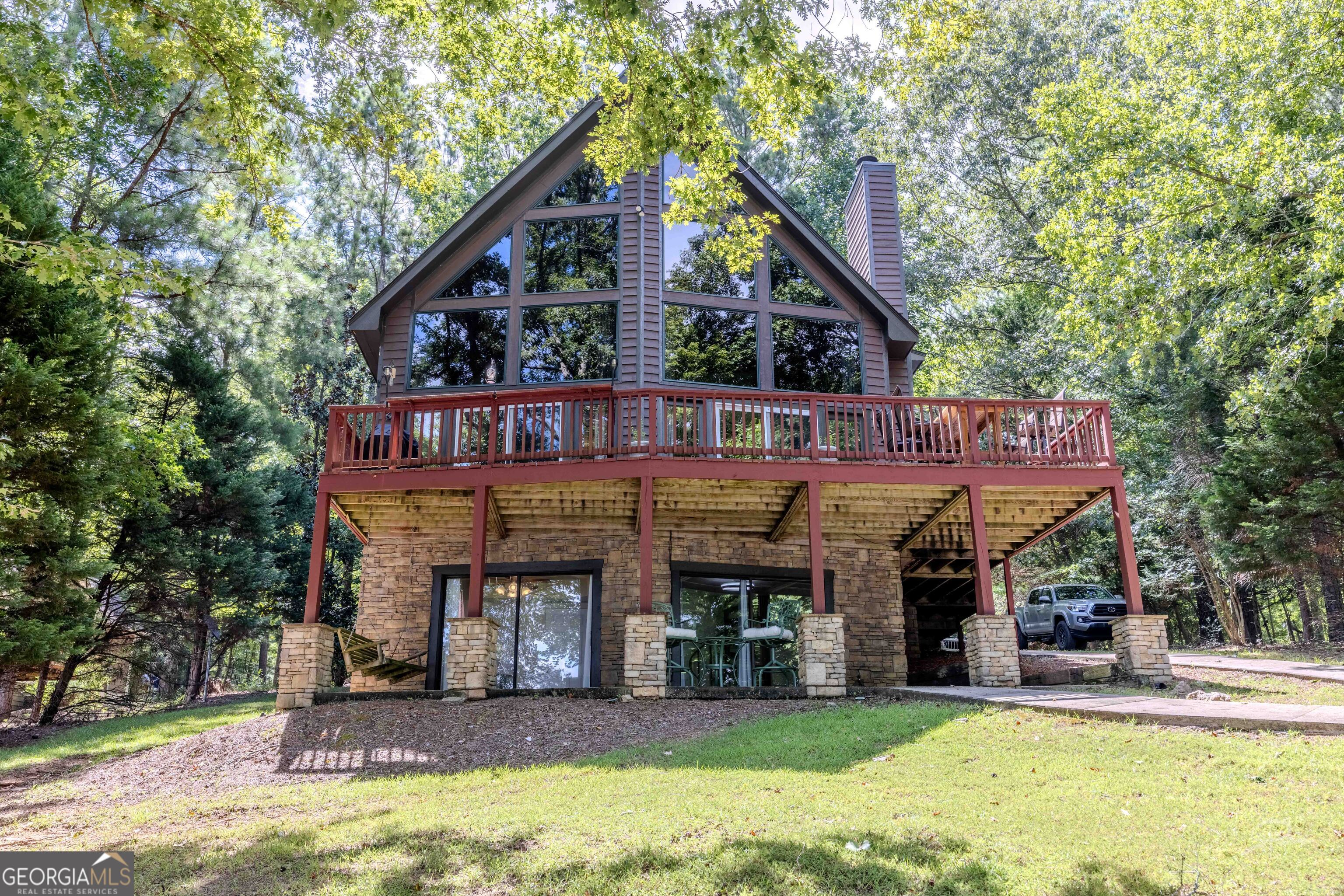 Charming A-Frame Lakefront Retreat on Lake Sinclair - Fee Simple Lot! Discover this perfect lake getaway! Nestled in a peaceful setting, this furnished home offers privacy & picturesque water views from every level. Step inside to find warm pine flooring throughout and a cozy living room w/ soaring wood-beamed ceilings & a beautiful stone wood-burning fireplace. The open-concept layout is ideal for entertaining, featuring a spacious kitchen with stainless steel appliances, ample storage, and seating at the large kitchen bar & the expansive dining table. One of the standout features of this home is its smart layout: a bedroom & full bath on each level provide comfort & privacy for all. The main-level master suite offers convenience, while the loft boasts a second master suite, a cozy sitting area with lake views-perfect for reading or relaxing-and space for a home office or workstation. Downstairs, the third bedroom is accompanied by a versatile bonus room that can serve as an extra sleeping area, game room, or additional living space. This level also includes exterior access via sliding doors and opens to a covered patio area, leading down a gently sloping yard to the lake. Outside, enjoy lakeside living with a single-stall boathouse featuring enclosed storage, and a covered dock area offering shade from the sun-perfect for taking in the gorgeous sunsets. Located near Oconee Springs Park in the desirable Holiday Shores community. There is a community boat ramp, pavilion/ fitness center/kitchen/event room. volunteer fire department, and a helipad. Don't miss out on this one!