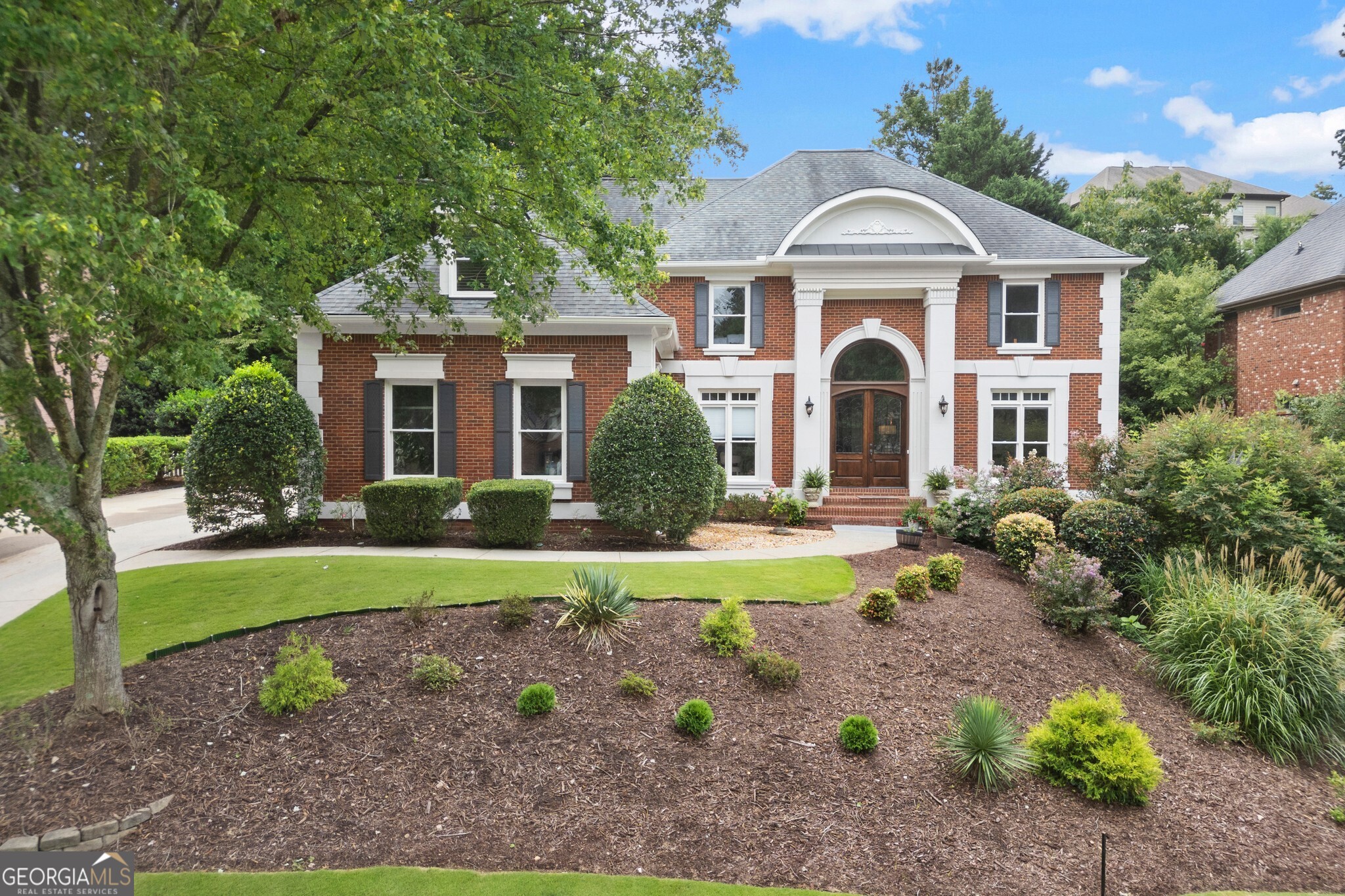 Welcome to this beautifully maintained brick home in the highly sought-after Glen Abbey community. This stately residence sits on a manicured lot with timeless curb appeal and a welcoming front entry. Step inside to a stunning two-story foyer with soaring ceilings and a dramatic staircase. A formal dining room sits to one side of the entry, and a spacious study or den is on the other, offering flexible space for entertaining or working from home. Beyond the foyer, the home opens into a grand living room with two-story ceilings, a cozy stone wood-burning fireplace, and built-in bookcases on either side. A wall of windows stretches to the height of the room, filling the space with natural light and offering serene views of the lush backyard. The kitchen is equally impressive and thoughtfully designed with a Forno double oven gas range, range hood, marble countertops, and a recently updated backsplash. A casual breakfast area sits just off the kitchen, ideal for everyday meals, and there is also a bar for additional seating. Also on the main floor is a generously sized bedroom with direct access to a full bathroom. This ensuite bath also serves as the guest bath for the main level, making it a convenient and private setup for visitors or multigenerational living. Upstairs, the expansive primary suite is a true retreat. Vaulted ceilings add architectural charm, and a cozy sitting area creates a perfect space to unwind. The ensuite bathroom offers two separate vanities, each with its own linen closet, along with abundant cabinet space and an oversized walk-in closet. Three additional bedrooms are located on the second floor. Two of these bedrooms share a Jack and Jill bathroom, while the third has access to its own full bath, providing a total of three bathrooms upstairs. The finished basement offers even more living space with multiple flexible areas for movie nights, games, crafts, or additional office space. Two more bedrooms and a full hall bathroom make this level perfect for guests, teens, or extended family. With seven total bedrooms and five full bathrooms, this home provides ample space and comfort for any lifestyle. Out in the backyard is space to enjoy the freshly landscaped grounds with a large deck, paved patio, and green grassy lawn. This peaceful and private outdoor space is perfect for hosting gatherings, dining al fresco, or relaxing after a long day. Thoughtful improvements include a newer roof and updated HVAC units. Located in the desirable Glen Abbey neighborhood, residents enjoy unmatched amenities. The recently renovated clubhouse includes entertaining spaces, a fitness center, swimming pool, a sport court, open athletic field with covered cabana, scenic community lake, walking trails, two playgrounds, and tennis courts with on-site tennis professionals. Glen Abbey also offers swim and tennis programs for all ages and skill levels. This home is ideally positioned near GA 400, the Big Creek Greenway trail, Avalon, and Historic Downtown Alpharetta, offering easy access to upscale shopping, fine dining, parks, and top-rated schools. With timeless style, abundant space, and access to exceptional amenities, this is the lifestyle you've been waiting for to call home.