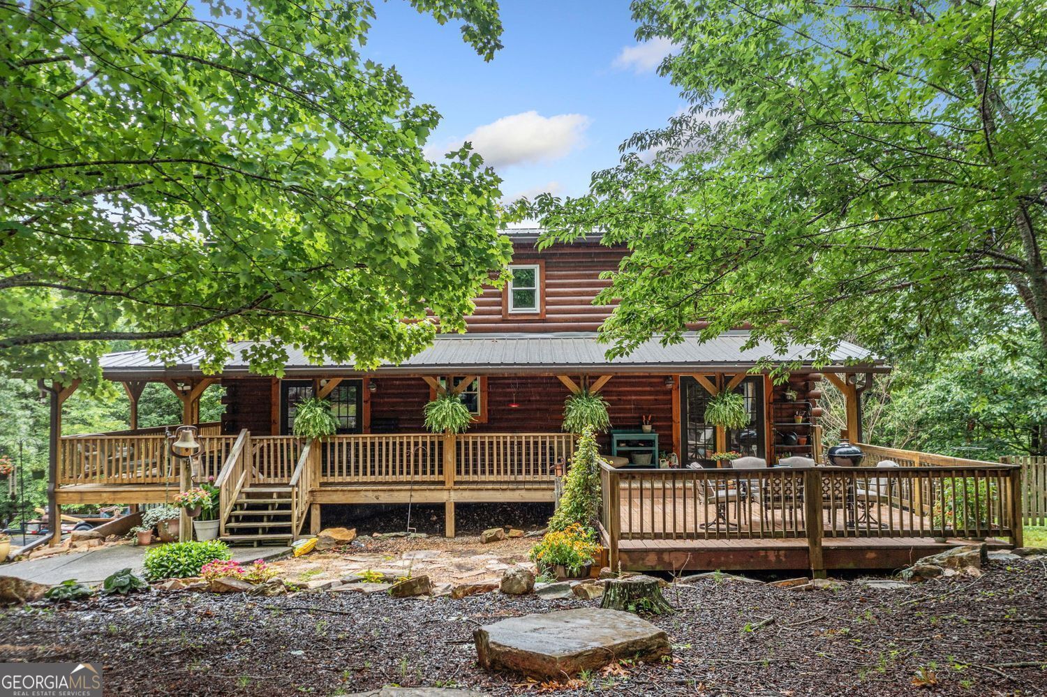 Tucked away behind a gated entrance on three wooded acres, this custom log cabin delivers the kind of peace and privacy that's getting harder to find. Every detail from the rocking-chair front porch and landscaped exterior to the wraparound deck, every inch invites you to slow down and settle in. Inside, the open-beam ceilings, wide plank walls, and hardwood floors set the tone, warm, rustic, and timeless. The main home features a spacious living area with soaring ceilings and skylights, a kitchen finished with granite counters, cherry-stained cabinets, and stainless steel Whirlpool appliances, and a main-level bedroom with a beautifully updated bath featuring a marble-topped double vanity and clawfoot tub. Additionally, there is a separate guest house featuring a full kitchen, living room with a bed and bath, making it perfect for extended family stays, rental income, or a tranquil office setup. It also includes a spacious storage room. And if you're bringing animals, the barn and fenced paddock are ready to go. Surrounded by other homes on acreage, this property blends privacy with a true sense of community just far enough out to feel like an escape, yet still within reach.