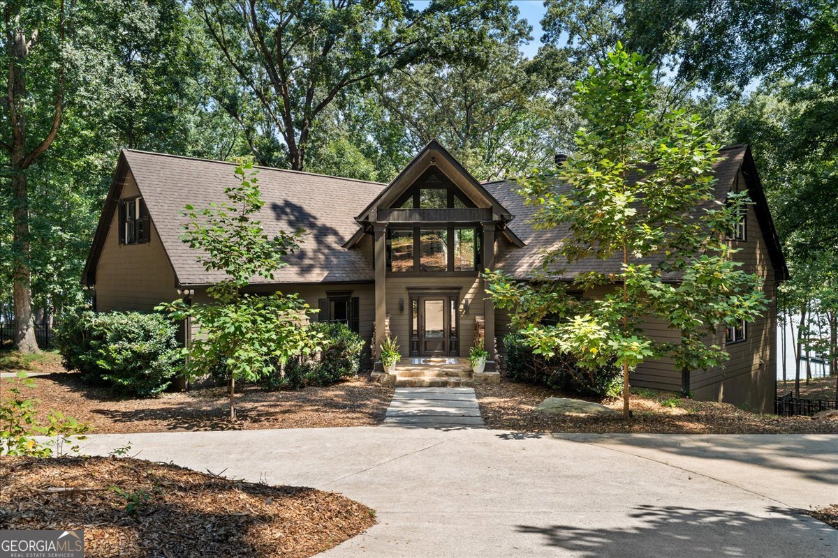 This stately yet charming 7-bedroom, 6-bathroom Lake Lanier estate with 7,025 sq ft sitting on more than 800 feet of shoreline, offering wide, deep-water views and direct access to the lake is sure to steal your heart. A classic ivy covered gate welcomes you in to the 1.33 acre property. The gentle backyard path to the lake leads to a 32x32 double-slip party dock with electricity, designed for easy days on the water. Situated in deep water and a coveted, quiet, no-wake cove with easy access to big water. Remodeled in 2017, the home was thoughtfully updated by the owner/architect to add space, comfort, and style on every floor. While conveniently located in Flowery Branch, the property backs onto over 20 acres of Corps land, creating an enjoyable private setting and a natural refuge for local wildlife-without the added upkeep or property taxes; complete with your own private beach. Inside, the home offers three primary suites, four secondary bedrooms, and two full kitchens, giving you flexibility for multigenerational living, hosting loved ones, rental opportunities, and full-time lake life. Natural light pours in from every floor-to-ceiling sliding glass window in the living and dining area, framing idyllic views of the cove, wooded land, and deer passing through. Features include oak hardwood floors, spa-quality showers with custom tile and stonework, all in a soothing palette. Nature provides plenty of light during the day and dimmable recessed lighting throughout the home illuminates the impressive architectural features in the evening. The lower level, with durable stained concrete floors, is well-suited for a game room, workshop, or garage and includes abundant storage for lake gear and supplies. An attached .75-acre lot adds even more opportunity. Already perc-tested for a 5-bedroom home and with a dock permit in hand for another 32x32 double-slip dock, it's ready for a guest house, rental property, pool, or multi-bay garage. 6680 Woodlake Drive is a rare combination of privacy, convenience, and prime lake access-an inviting place to gather, recharge, and enjoy the best of Lake Lanier.