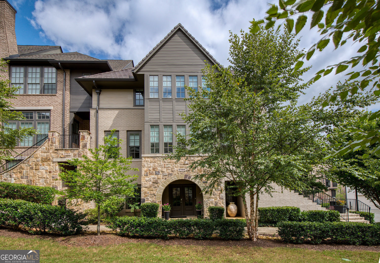 Luxury, Location & Convenience. Welcome to 6766 Cadence Boulevard, nestled in the sought-after Ashton Woods development of Aria North. This custom-designed, wide end unit showcases the coveted Ashton Woods Signature Domingo floorplan, enhanced with a covered front entrance, elongated driveway, extra end-unit windows, distinctive architectural details, a finished terrace level, and peaceful views of the front courtyard. Offering 3,170 square feet, this residence is a rare gem-delivering the feel of a single-family home with the ease of low-maintenance living. Impeccably maintained, spacious, and thoughtfully designed, it's the perfect balance of comfort and sophistication. Inside, discover 3 bedrooms, 3 full bathrooms, and 1 half bath. The gourmet chef's kitchen features stunning stone countertops, an upgraded 6-burner range, premium KitchenAid stainless steel appliances, a pot filler, striking pendant lighting, and generous barstool seating-perfect for entertaining. The adjacent dining room, complete with an upgraded chandelier, sets the stage for memorable dinner parties. The great room offers a custom-designed fireplace flanked by built-in cabinetry and is bathed in natural light. Step outside to the covered back deck, an ideal spot to savor the upcoming crisp fall evenings. Throughout the home, upgraded hardwood floors and lighting fixtures provide a consistent sense of style and quality. Upstairs, the inviting owner's suite is a true retreat. The spa-like bathroom boasts dual vanities, an oversized upgraded shower with built-in bench, and a soaking tub. A second upper-level bedroom also enjoys its own private en-suite bath. Custom Restoration Hardware shades and blinds are installed throughout the home, and the entire property is wired for speakers + smart-home integration. The finished terrace level reveals a hidden third bedroom and full bath, plus an additional gathering space with a brick accent wall, custom built-in bar, and cabinetry. The spacious garage-equipped with an electric car charging station-is accessed via a private alley, while the extended driveway offers rare additional parking. Located just minutes from GA-400 and with close proximity to I-285, this home offers unmatched convenience. Aria North residents enjoy exceptional amenities, including two pools, a fitness center, clubhouse, club room, and a 12-acre park. You'll also love strolling to the shops and restaurants in Aria Village. This is your opportunity to live in true luxury-schedule your private showing today!