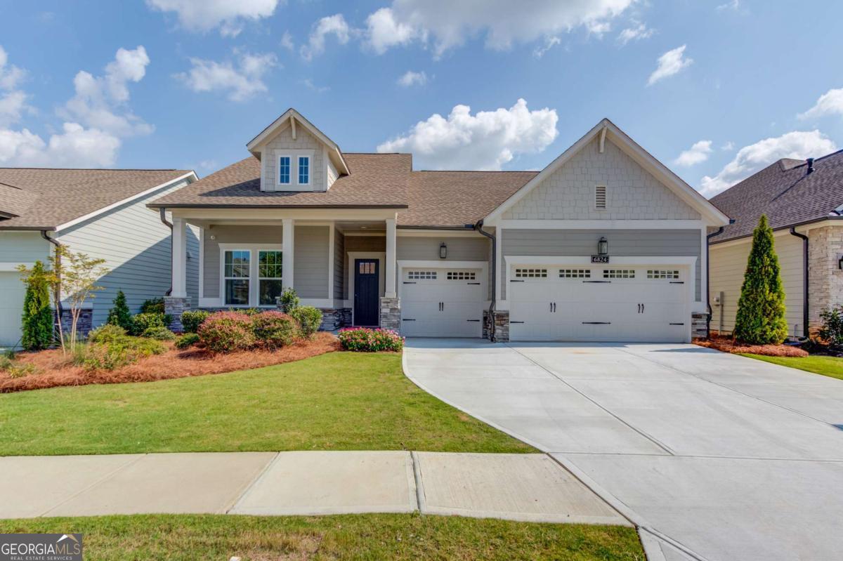 Never-lived-in former model home in The Retreat at Sterling on the Lake, offering luxury, comfort, and breathtaking views with all the bells and whistles. Built in 2020, this stunning 3-bedroom, 3-bath Craftsman-style residence combines thoughtful design with top-tier finishes across a spacious 2,587 SQ FT single-level layout. Designed to impress, the home features custom accent walls in the living room, guest bedroom, and office, wide-plank 5" hardwood flooring, custom lighting, and elegant trim details throughout. The open-concept living space is anchored by a 12-foot sliding glass door that fills the room with natural light and opens to an extended covered patio-the perfect spot to enjoy sweeping views of Flowery Branch. The chef's kitchen includes quartz countertops, premium cabinetry, and seamless flow into the dining and living areas-ideal for both entertaining and everyday living. The primary suite features a spa-inspired bath and a custom walk-in closet system for maximum organization and luxury. Additional highlights include a 3-car garage with extra storage and permanent walk-up attic stairs, a whole-home sound and security system, and a spacious laundry room with built-in sink and storage just off the garage entry. Located in The Retreat, a private 55+ enclave within Sterling on the Lake, residents enjoy access to an exclusive clubhouse featuring a gym, resort-style pool, pickleball courts, and a community gathering space. As part of the larger Sterling on the Lake community, you'll also have access to lakes, walking trails, events, and a full-time lifestyle director coordinating clubs and activities.Just minutes from Cherokee Bluff Park, the local library, and convenient to grocery stores, Target, Home Depot, I-85, and I-985, this home offers the ideal combination of luxury living and everyday convenience. This is your last opportunity for a brand new construction home in the fully completed Retreat at Sterling on the Lake-this beautifully upgraded model is move-in ready and better than new.