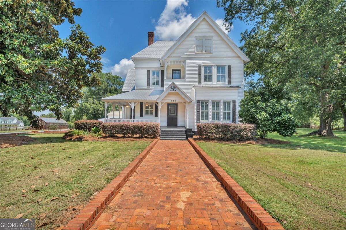 Discover the perfect blend of privacy, charm, and convenience with this beautifully updated 1887 farmhouse located minutes from I-75 creating an easy drive to Macon or Atlanta. Full of timeless character, this two-story gem welcomes you with tall, wide front porches perfect for rocking chairs and morning coffee. Inside, you'll find soaring ceilings, hardwood floors, an enormous open kitchen with endless storage alongside the grand dining room for friends and family to gather. The primary bedroom with ensuite is located on the main floor, and the beautiful staircase leads to a spacious upstairs with three bedrooms and a full bathroom. The home has been thoughtfully updated, including a tankless water heater and brand new Berridge Victorian metal shingled roof, and a 3-car detached garage with room for the golf cart or ATV. Nestled on 5 acres of flat usable land that includes fenced pastureland, this home offers an ideal setting for gardening enthusiasts: raised bed gardens with irrigation and a Yoderbilt greenhouse with electricity, water and gas heat. Enjoy mature fig and pecan trees, blueberries, and muscadine vines. The new 20x40 metal barn, workshop areas and outbuildings are ready to support your hobby farming or homesteading goals. This is more than just a place to live, this is a place to enjoy the peace and quiet of your own private retreat.