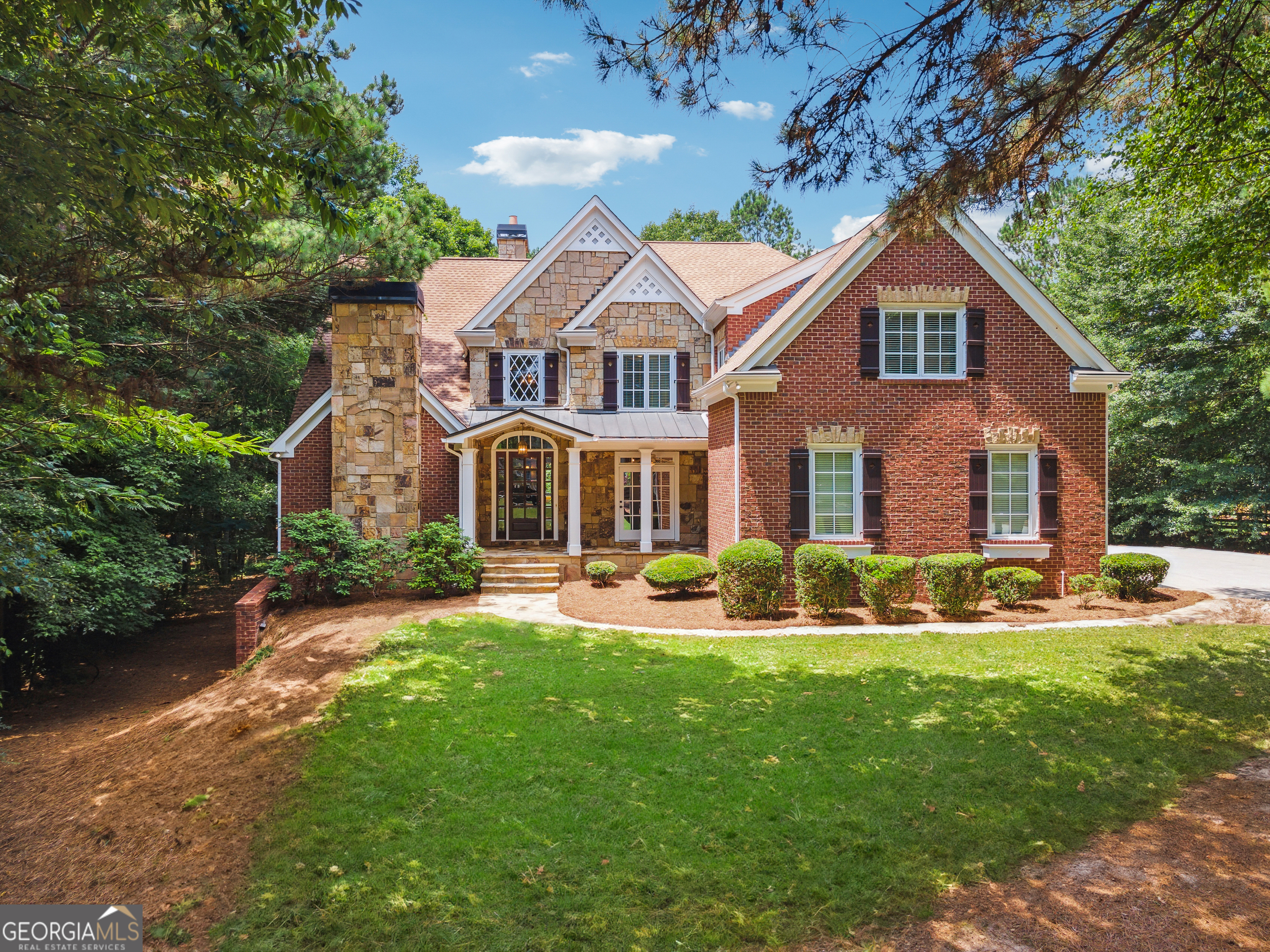 Nestled within the beautiful gated community of Blackberry Ridge, this expansive 2-acre estate home offers a seamless blend of luxury, privacy, and convenience. Located in Cherokee County with the benefit of lower taxes and zoned for the highly desirable Creekview High School, this residence showcases timeless finishes and a thoughtfully designed, spacious layout that epitomizes refined living. As you approach, you'll be captivated by its stately four-sided brick and stone construction, highlighted by a charming stone front porch and a spacious private yard. Inside, the main level exudes elegance and functionality, featuring solid mahogany wood floors that add warmth and sophistication. The living room, with its soaring vaulted ceilings and a striking stone fireplace with a gas starter, creates an inviting atmosphere. Adjacent to this space, the gourmet kitchen is a true culinary haven, boasting granite countertops, a gas range, a large walk-in pantry, and a convenient butler's pantry. Overlooking the spacious keeping room-complete with a cozy stone gas fireplace-this kitchen is designed for both everyday living and effortless entertaining. The primary suite on the main level serves as a luxurious retreat, featuring a sitting room with a stone fireplace and vaulted ceilings that enhance the home's distinctive character. Past dual walk-in closets, the spa-like primary bath impresses with a Jacuzzi tub, an oversized dual-head shower, and a coffered ceiling that adds a touch of grandeur. An additional ensuite guest bedroom on the main level provides comfort and privacy, making it ideal for in-laws, visitors, or a teen suite. The upper level offers exceptional flexibility, featuring three ensuite bedrooms, a large fireside office/study, and a bonus room-perfect for use as a playroom, home office, or an optional sixth bedroom. Designed for entertaining, the home's three-sided walk-out terrace level is finished to the same high standards as the main level. This space includes a full wet bar kitchen with bar seating, custom-made backlit counters, and a stone fireplace in the sitting room. The game room, pool table area, and theater room-complete with a raised ceiling and sound system-offer endless entertainment possibilities. A full bath with laundry and ample extra storage space complete this level. Notable features of this remarkable home include a circulating hot water system, a cedar closet, encasement windows, five fireplaces, dual in-line water heaters, and laundry rooms on all three levels. The home is also equipped with a central vacuum system. The oversized three-car garage provides ample space for vehicles and equipment, with additional storage at the front. Two of the three HVAC units were replaced in 2021/2022 for added efficiency and comfort. Beyond the home itself, the location is another significant highlight. Situated just five minutes from 7 Acre Barngrill, Publix, and Scottsdale Farms, the property offers easy access to daily conveniences and dining options. It is only 15 minutes from downtown Milton's Crabapple district, known for its charming atmosphere and community events. For those seeking a vibrant city lifestyle with effortless commuting, downtown Alpharetta, Avalon, and GA-400 are just 20 minutes away, offering premier shopping, dining, and entertainment opportunities.