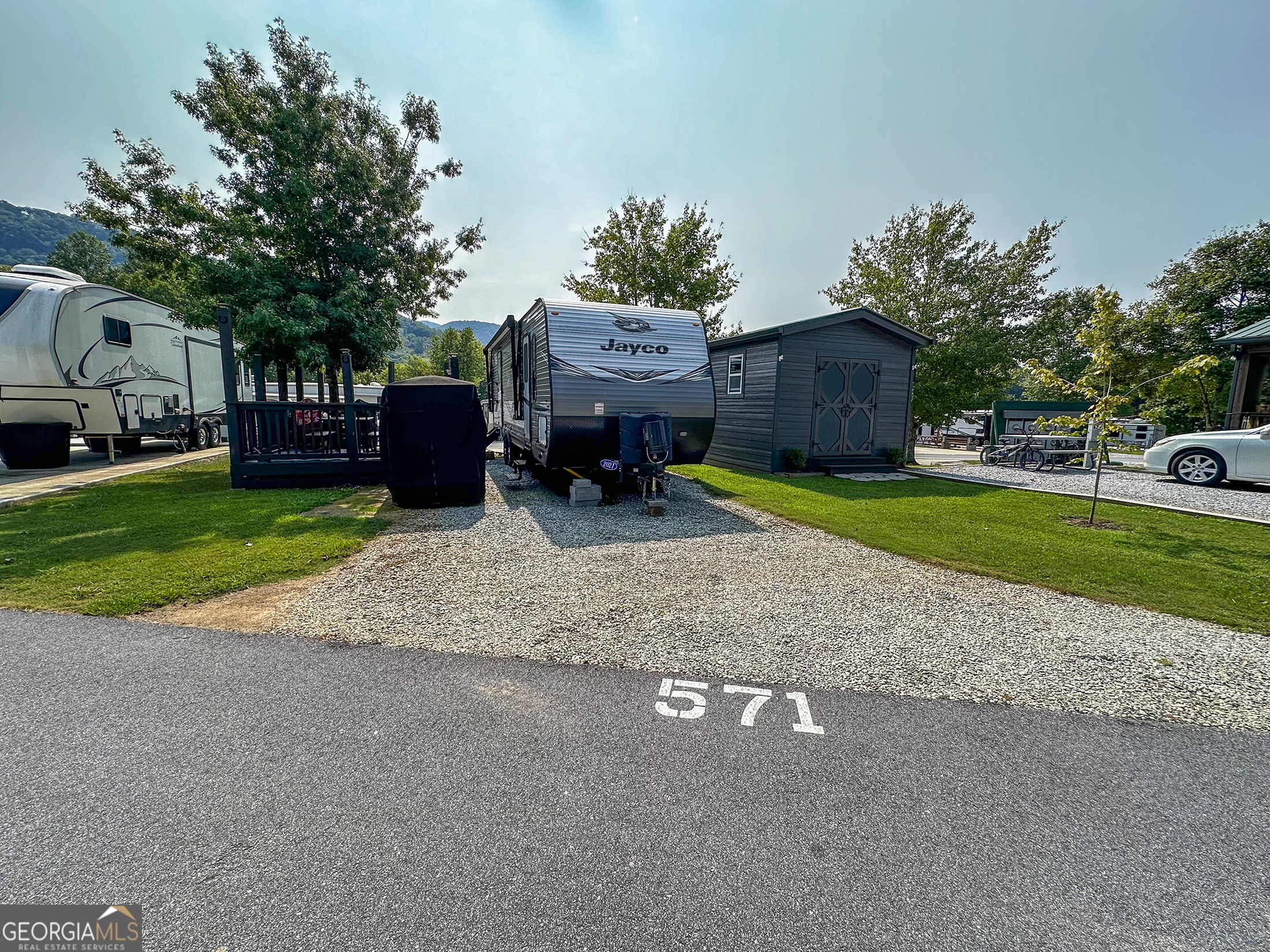 Lot 571 River Vista Dr. sits in River Vista RV Resort in the North Georgia Mountains near Dillard, GA, close to Clayton, GA, Highlands, and Franklin, NC. Enjoy amenities like an outdoor pool, indoor hot tub, dog park, clubhouse, exercise room, and playground. The lot features a porch for relaxing with friends amid cool mountain air and views. Experience the RV lifestyle with mild summers, vivid fall colors, and nearby activities, just 5 miles from Sky Valley Country Club. Camper sold separately.